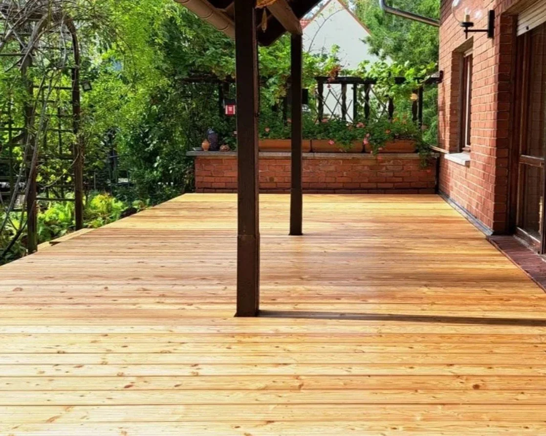 Ein Holzterrasse vor einem roten Backsteinhaus mit Garten und Grünanlagen im Hintergrund.