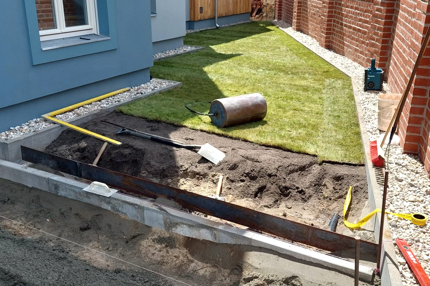 Rasen wird angelegt, hier als Rollrasen. Die zuvor notwendigen Erdarbeiten sind sichtbar.