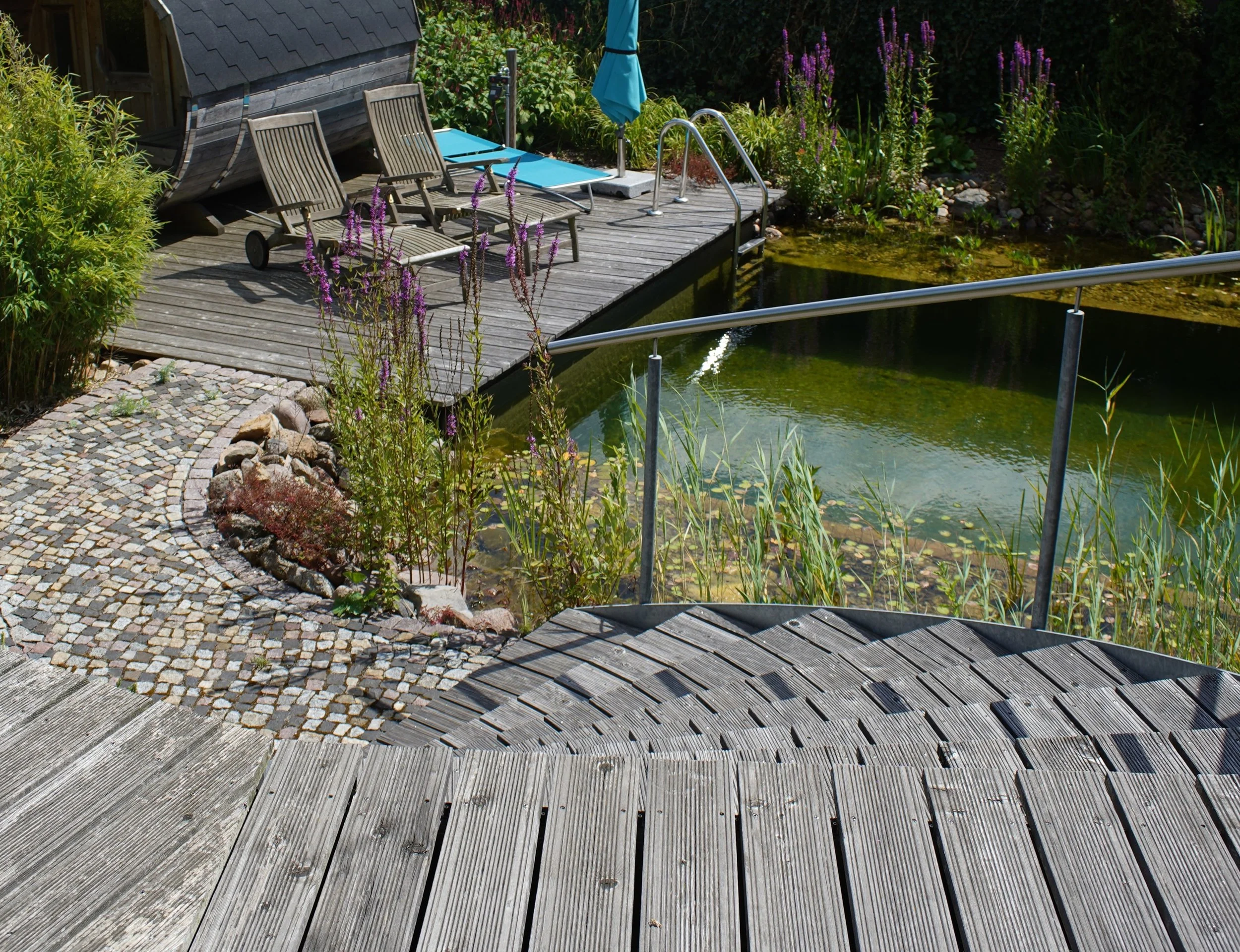 Holzterrasse mit Geländer über einem kleinen Schwimmteich.