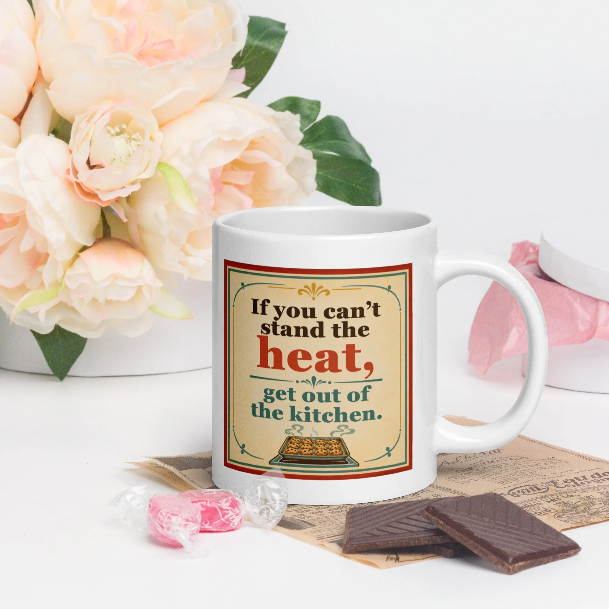 Lifestyle photo of the “If you can’t stand the heat, get out of the kitchen” mug on a tray with flowers and treats.