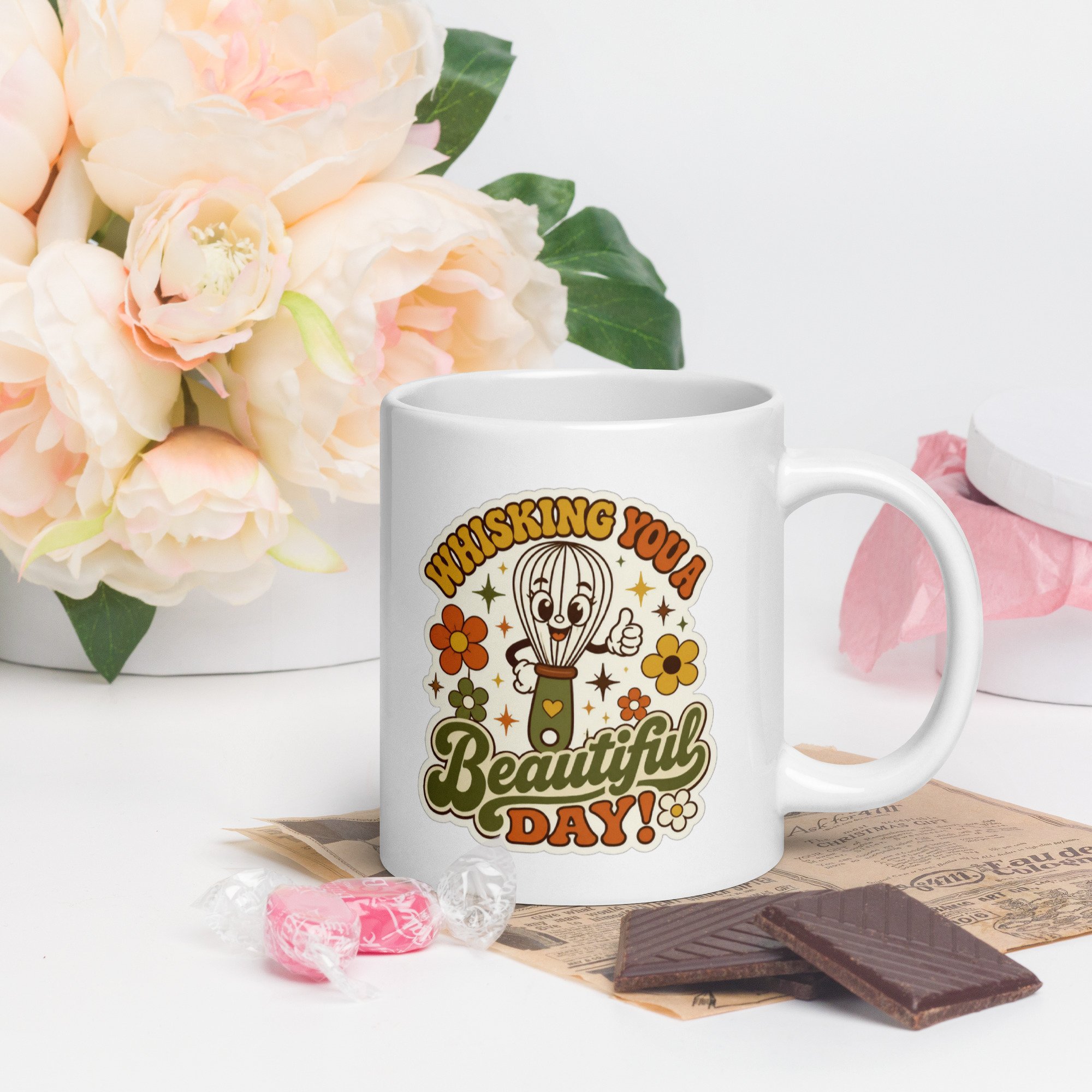 Styled photo of the retro baking mug with “Whisking You a Beautiful Day” whisk design on a table with flowers and baking props.