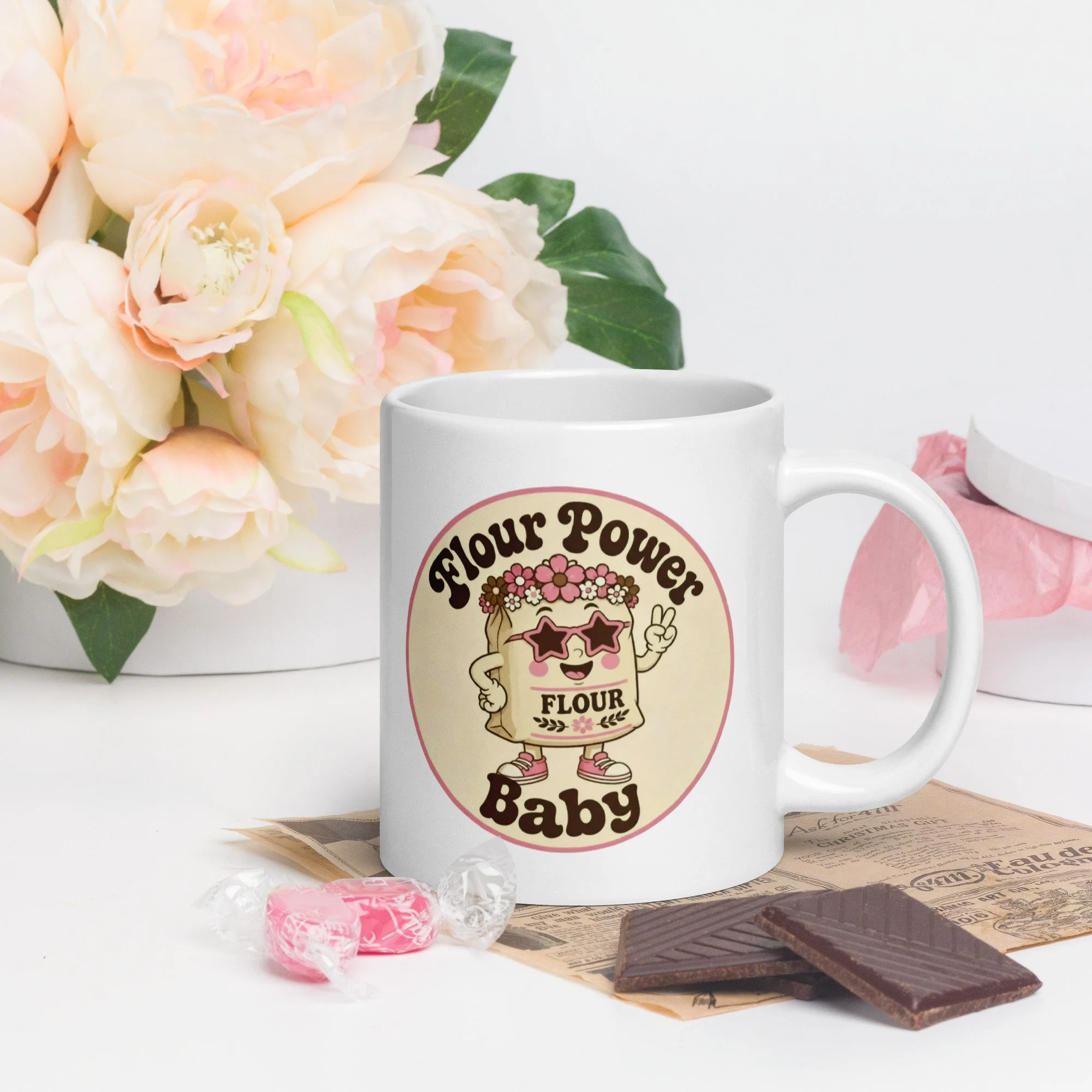 Styled photo of the “Flour Power Baby” retro baking mug on a table with flowers and baking props.