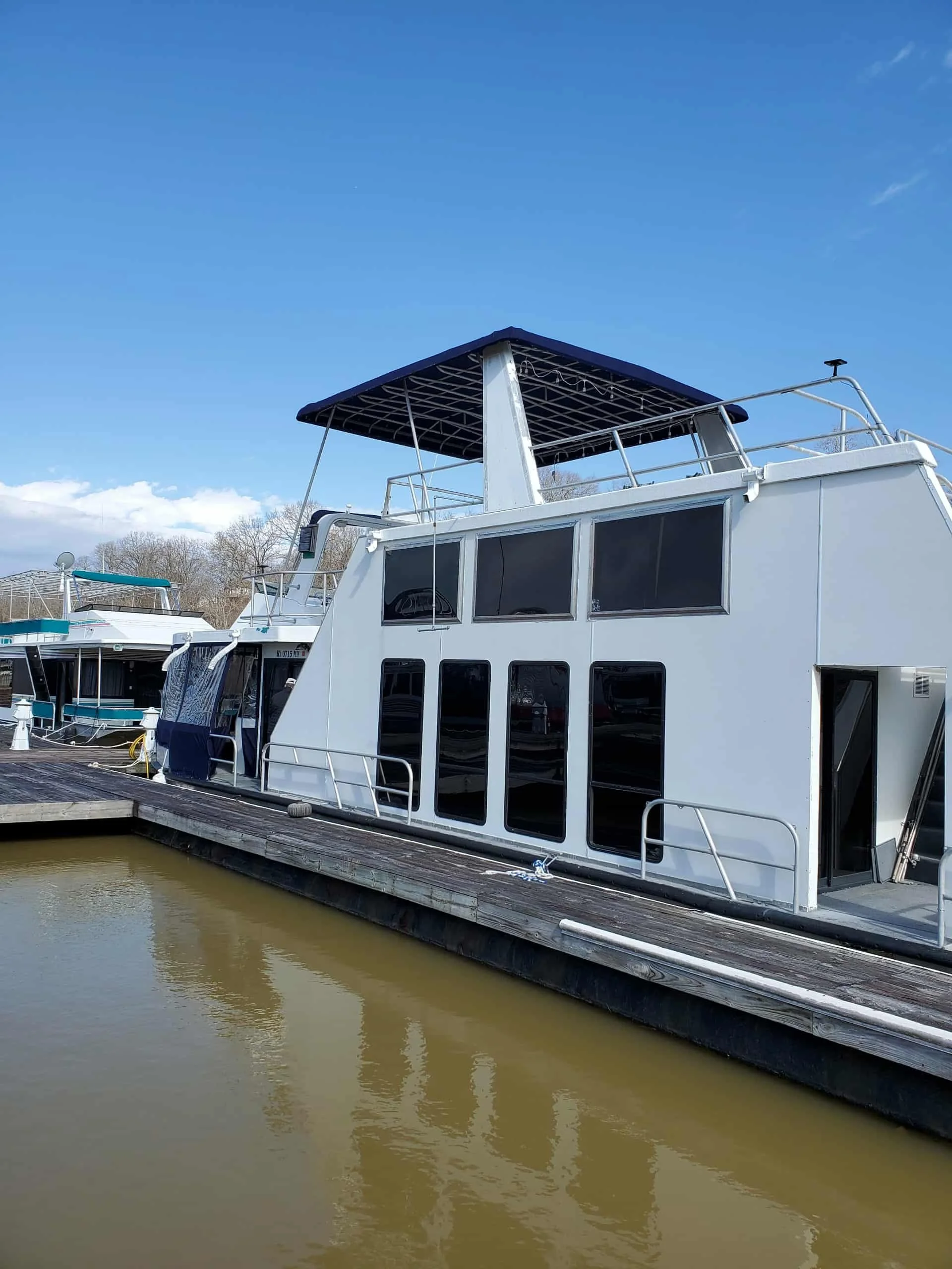 White houseboat docked at a marina with a blue sky in the background.