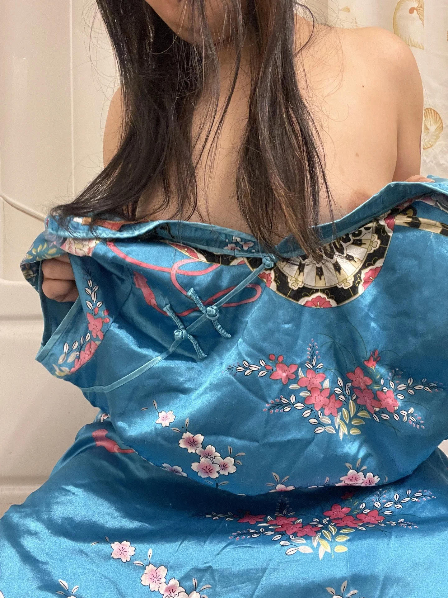 Person holding a floral-patterned blue satin robe, partially revealing their shoulder and chest.