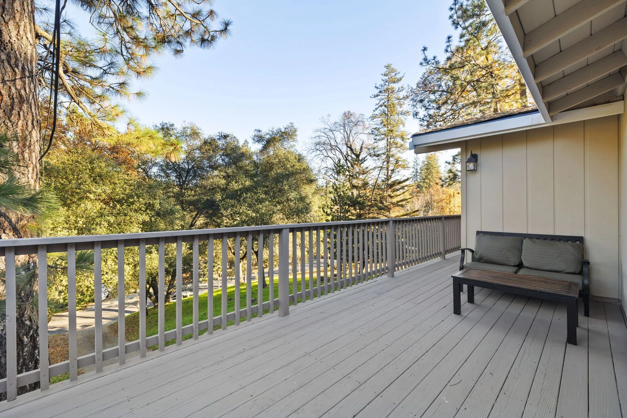 Empty balcony with a bench and pillows overlooking a lush green backyard with trees.