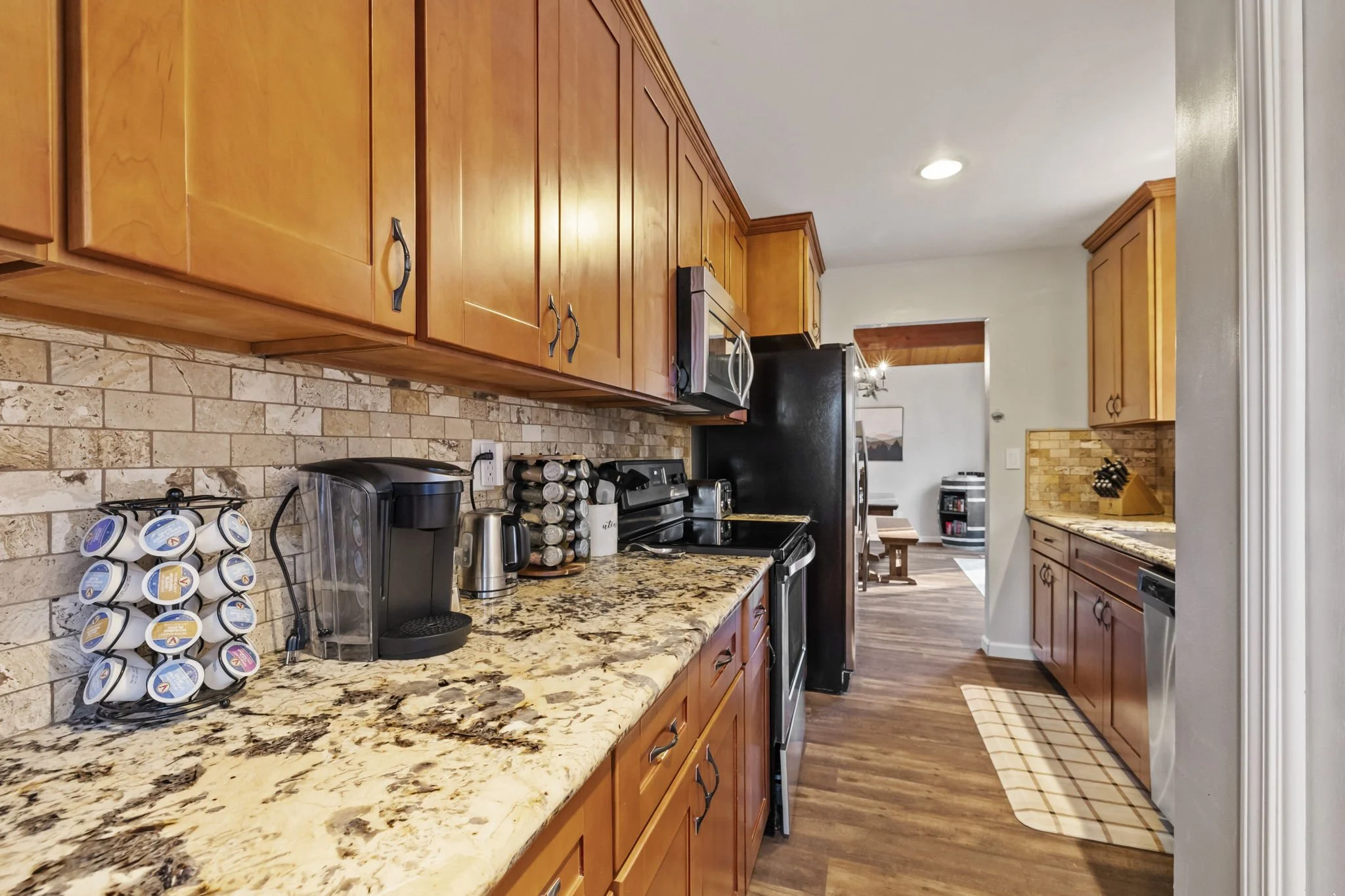 Kitchen with wooden cabinets, granite countertops, a coffee maker, a spice rack, a stove, microwave, and dishwasher, with hardwood floors.