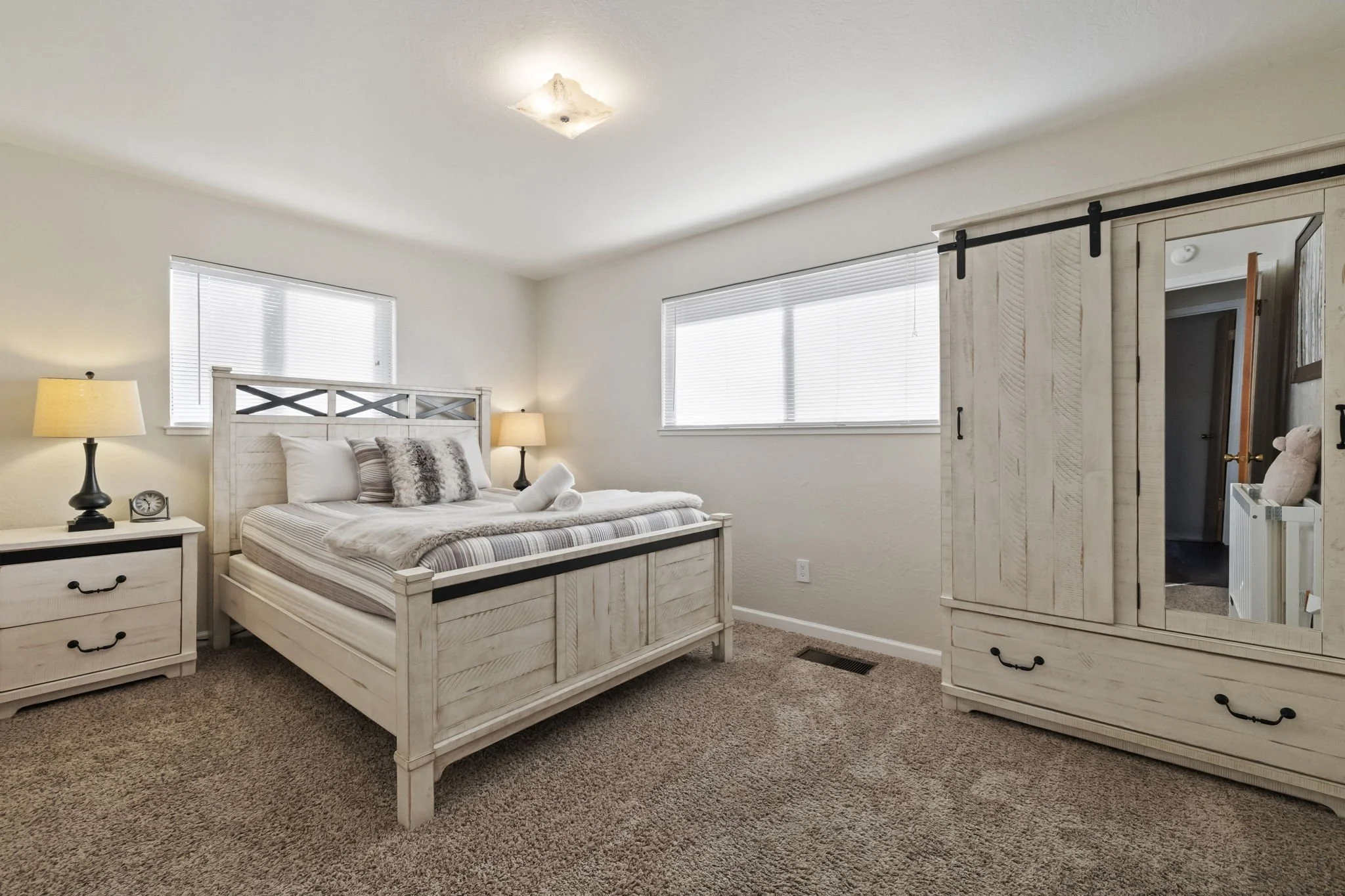 A bedroom with a bed, nightstands, lamps, a window, and a wooden wardrobe with a mirror.