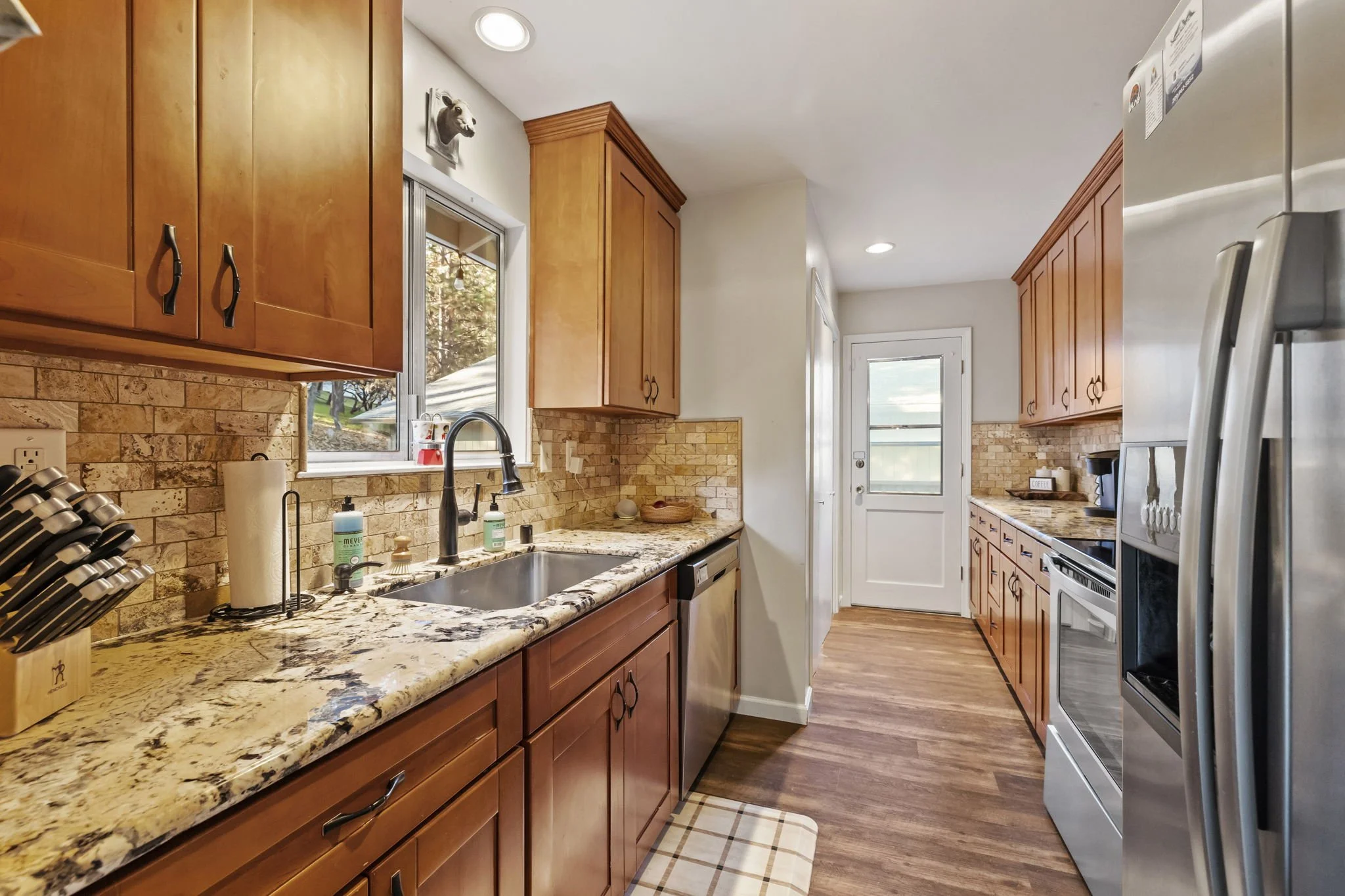 Kitchen with wooden cabinets, granite countertops, brick backsplash, stainless steel appliances, and a window above the sink.