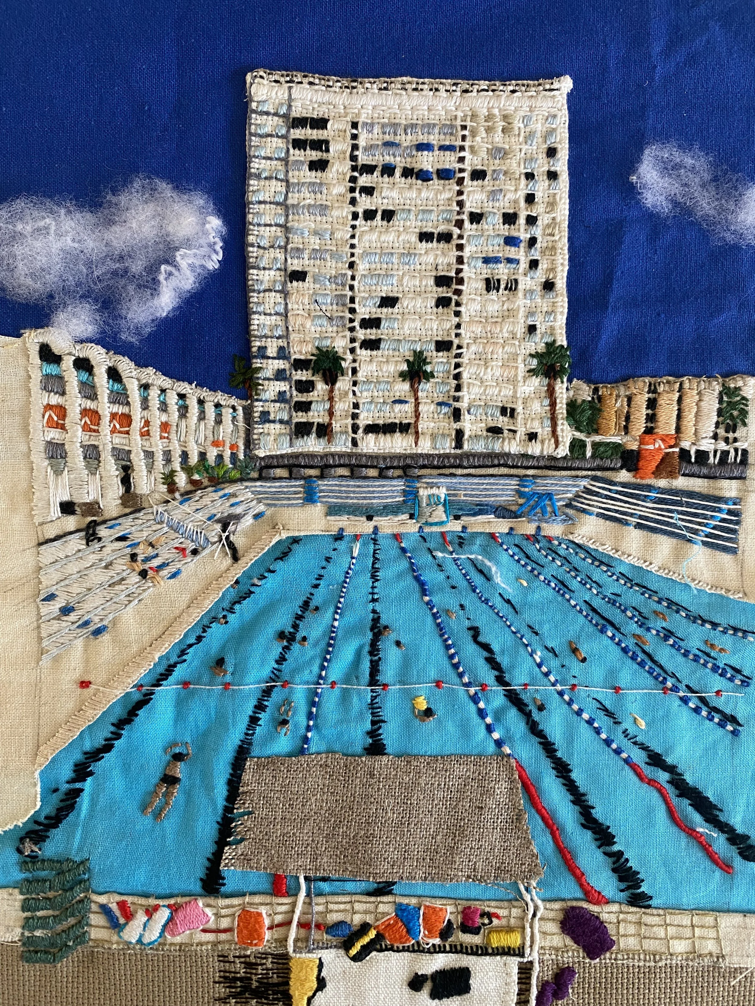 Embroidery of a cityscape with a large high-rise building, palm trees, and pool area, on blue fabric background.