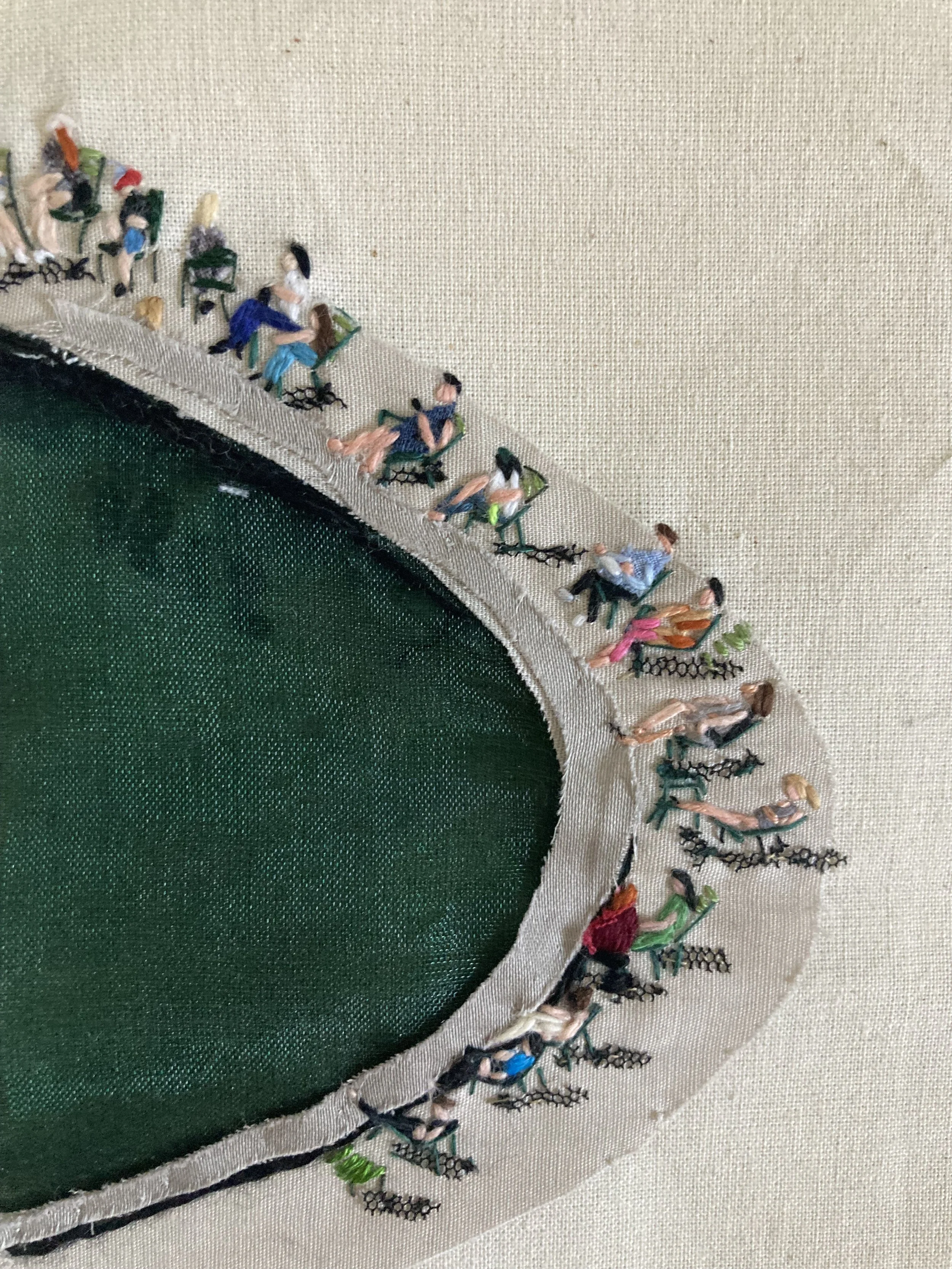  embroidery of people sitting around the edge of a green, oval-shaped object.