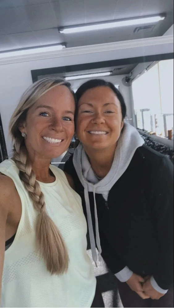 Two women smiling and taking a selfie in a gym or sports facility.