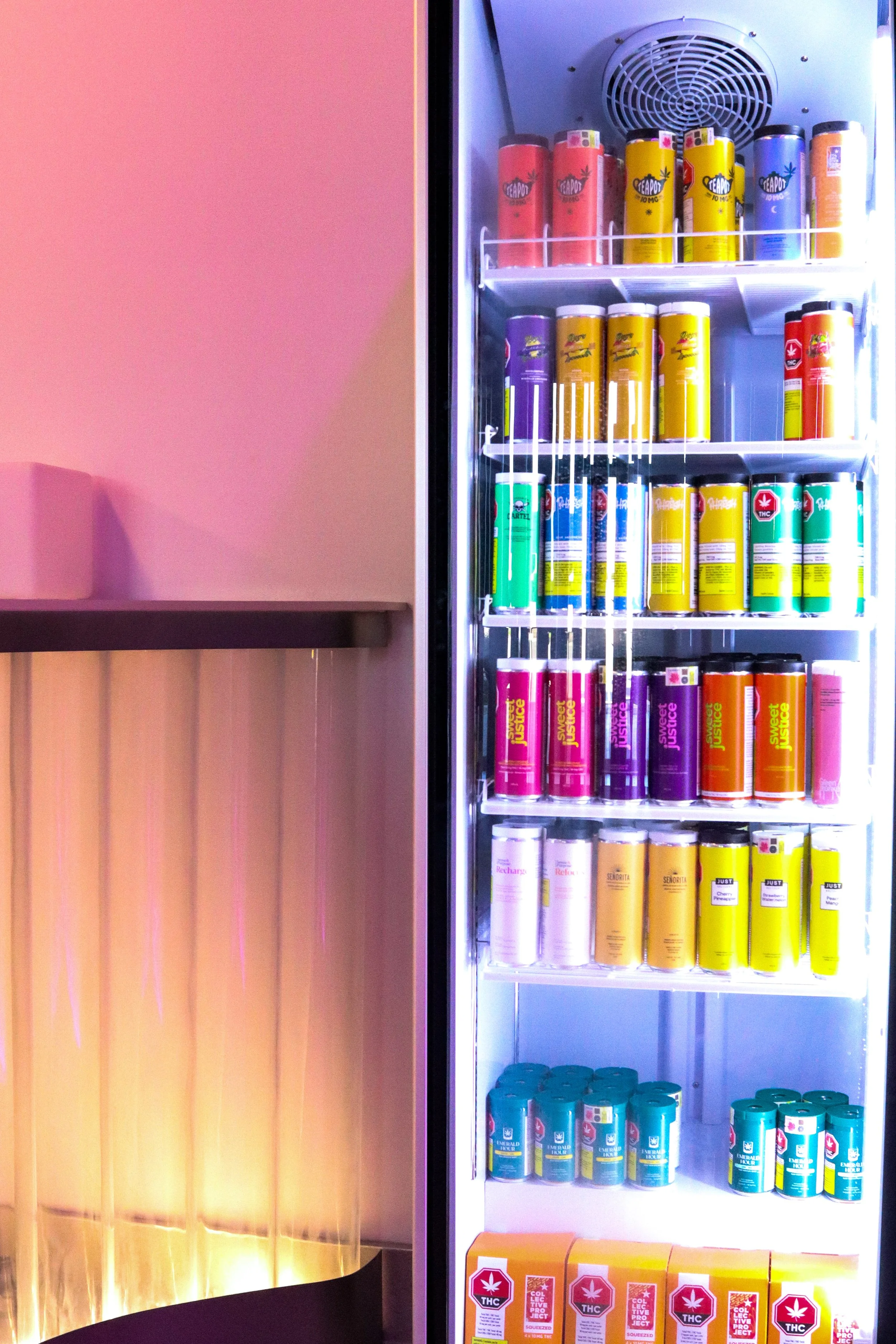 Refrigerator with multiple shelves of colorful cans and boxes of cannabis products, including THC and CBD labels.