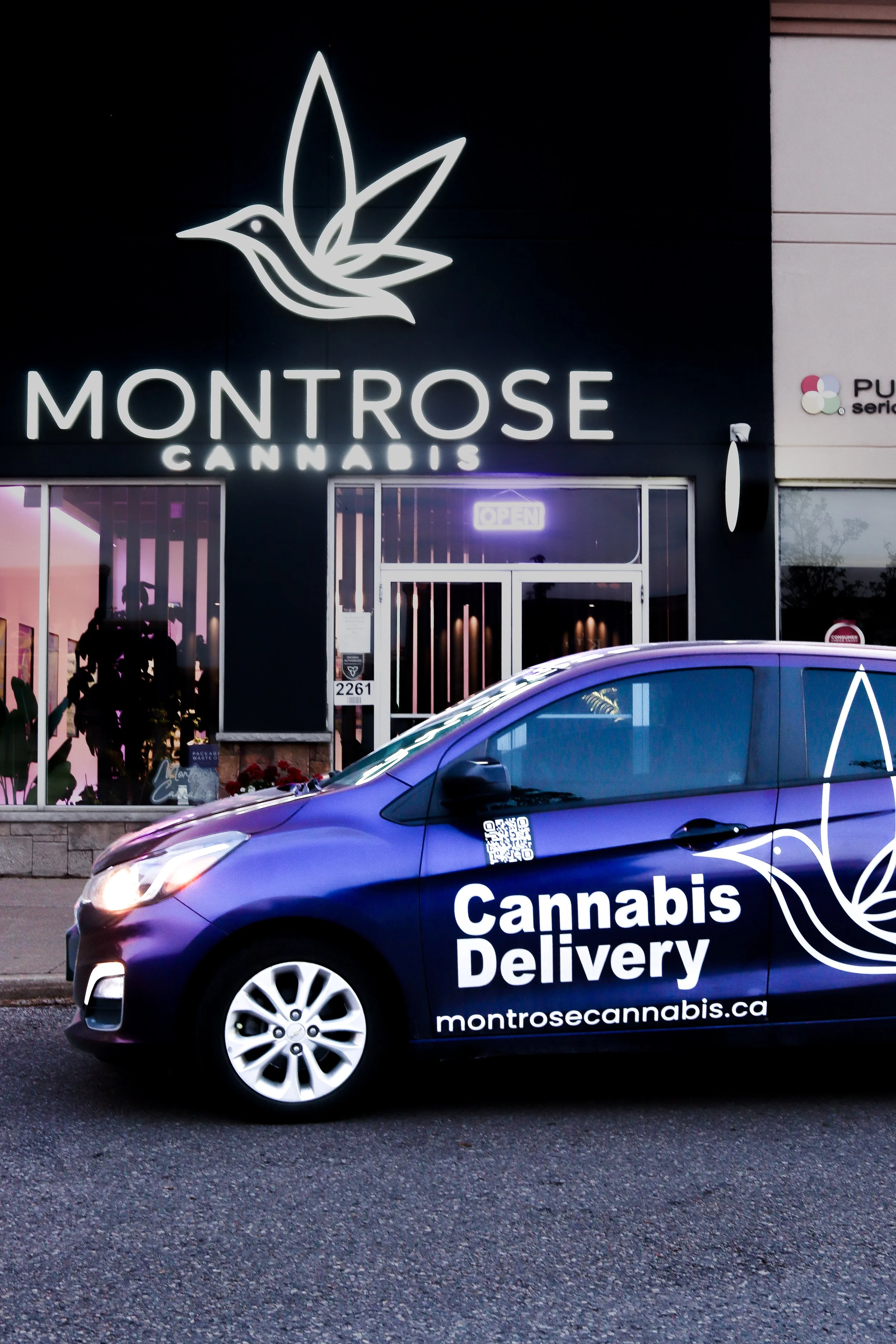 A storefront with a neon sign that says "OPEN" and features a logo with a hummingbird and leaves. A parked car in front has branding for "Montrose Cannabis Delivery" with a web address, and a purple and white background.