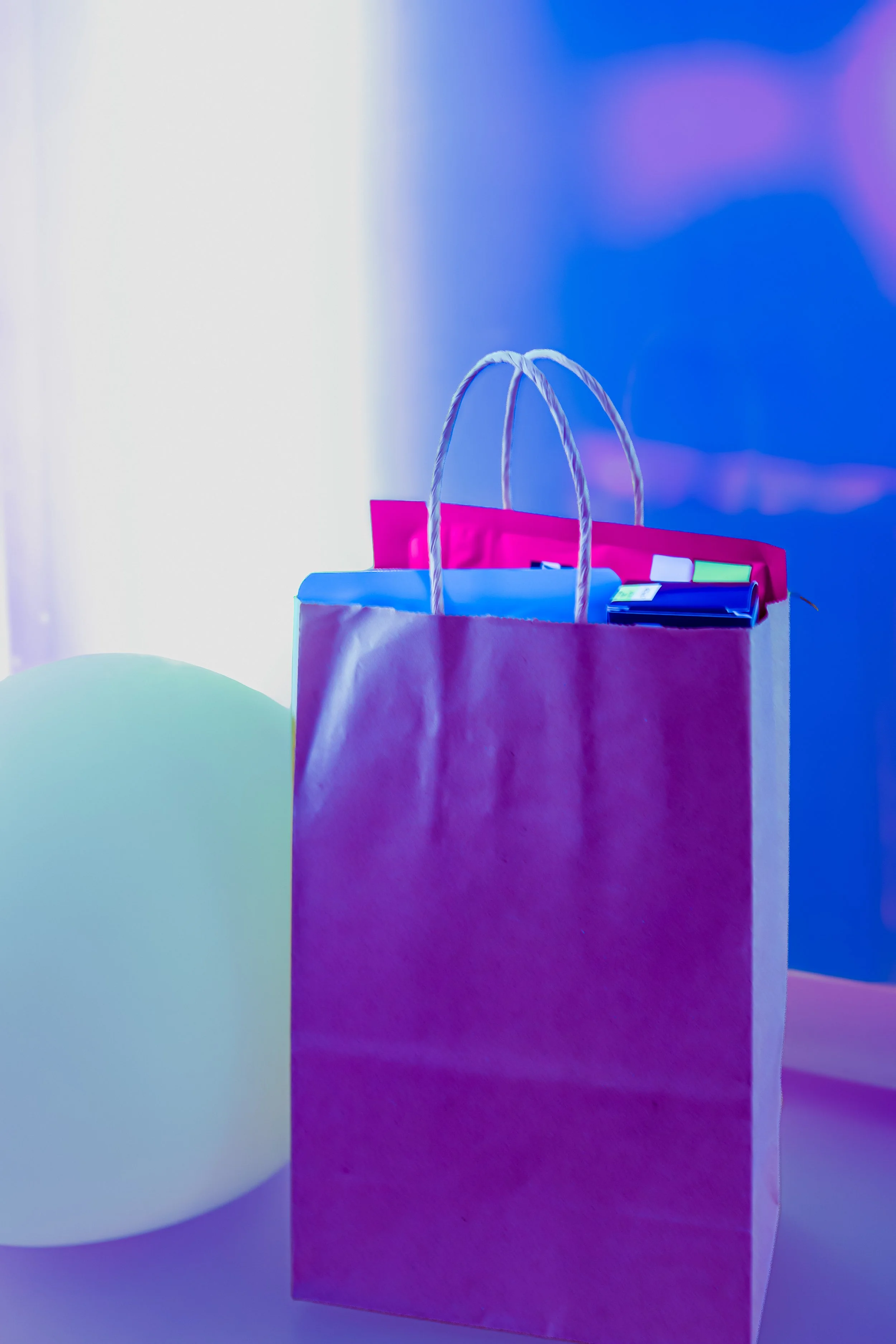 A pink shopping bag with white rope handles, with some papers and a smartphone inside, against a colorful abstract background.