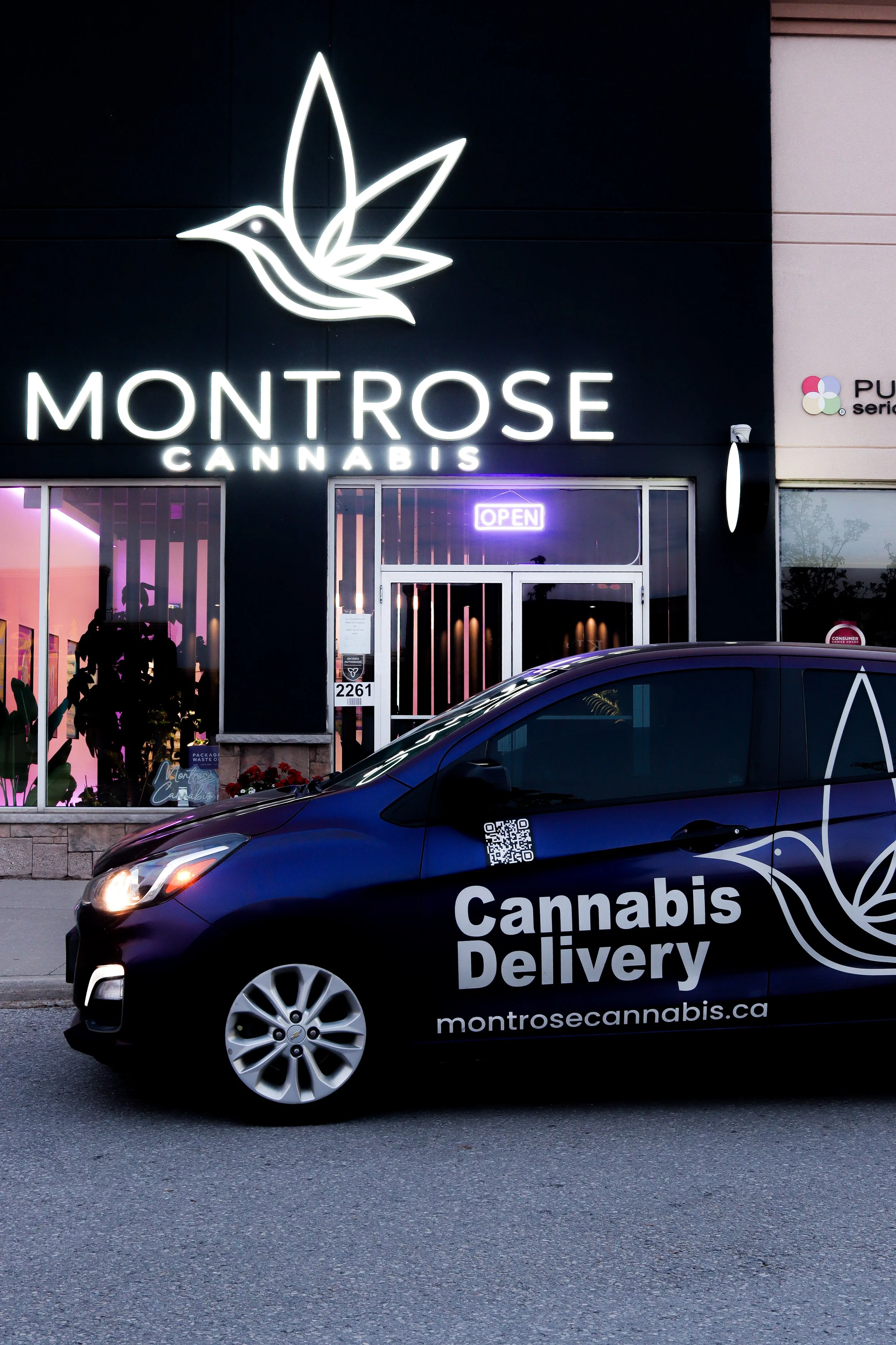 Black van with white lettering reading 'Cannabis Delivery' and the website montrosecannabis.ca, parked in front of a cannabis store with neon 'Open' sign and storefront sign reading 'Montrose Cannabis.'