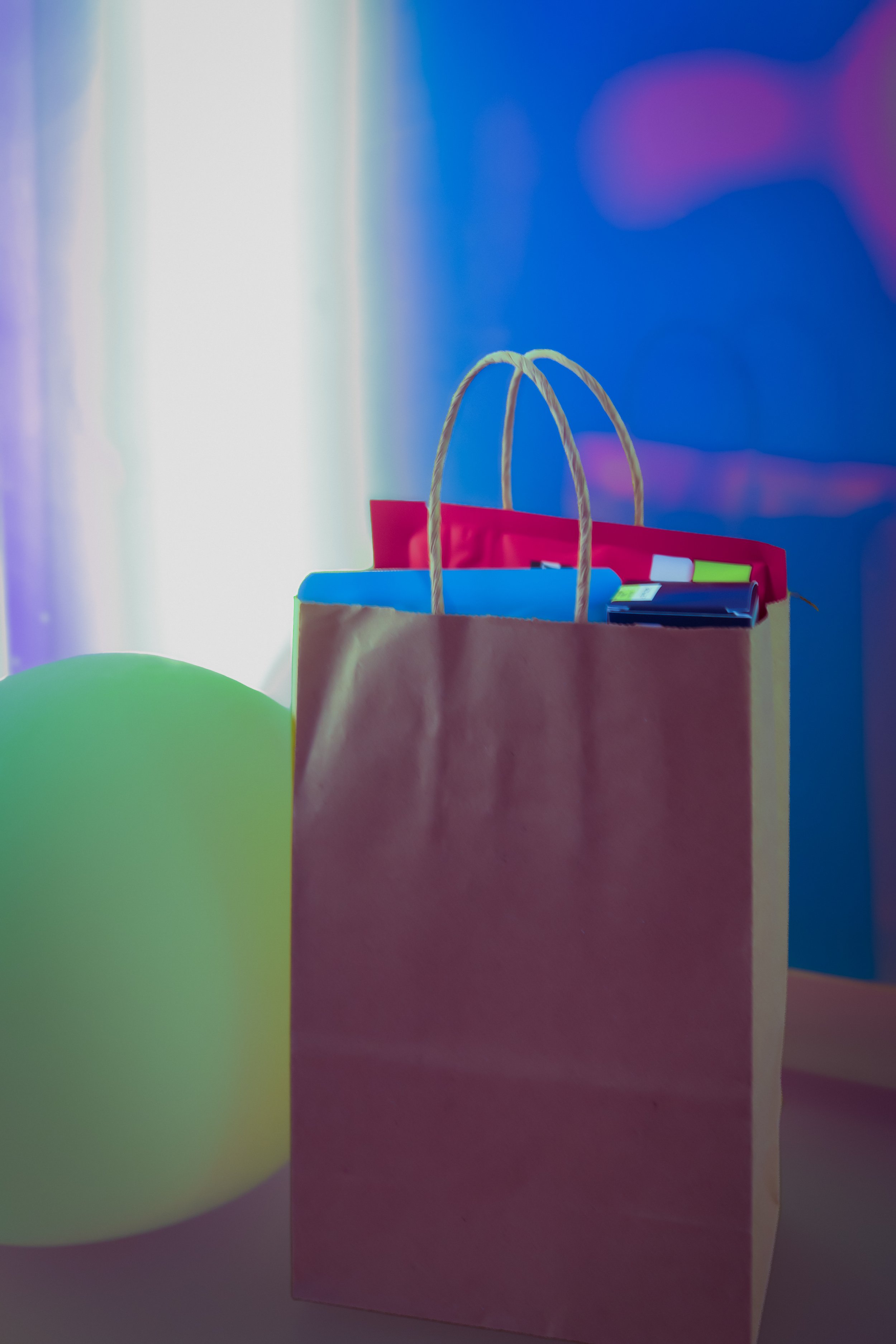 Colorful shopping bag with rope handles and assorted items inside, placed on a surface with a soft, blurred, colorful background.