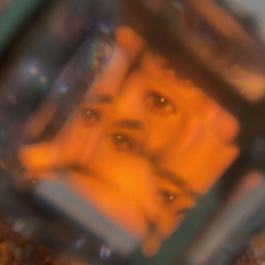 A blurred close-up of a computer or phone screen displaying a woman with long dark hair making an 'OK' gesture with her hand.