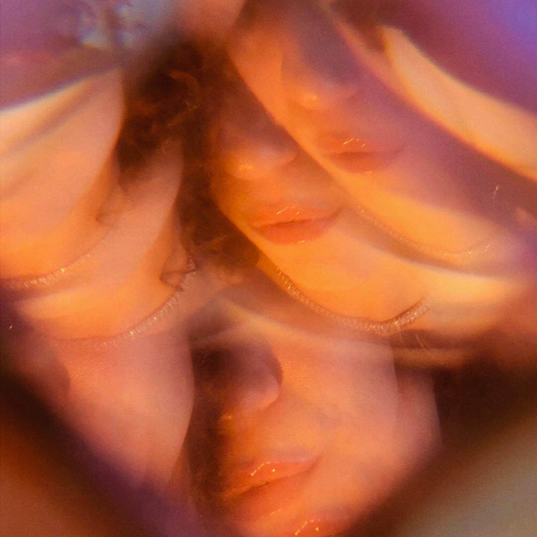 A blurred, artistic photo of two women with closed eyes wearing thin necklaces, with warm lighting creating an abstract effect.