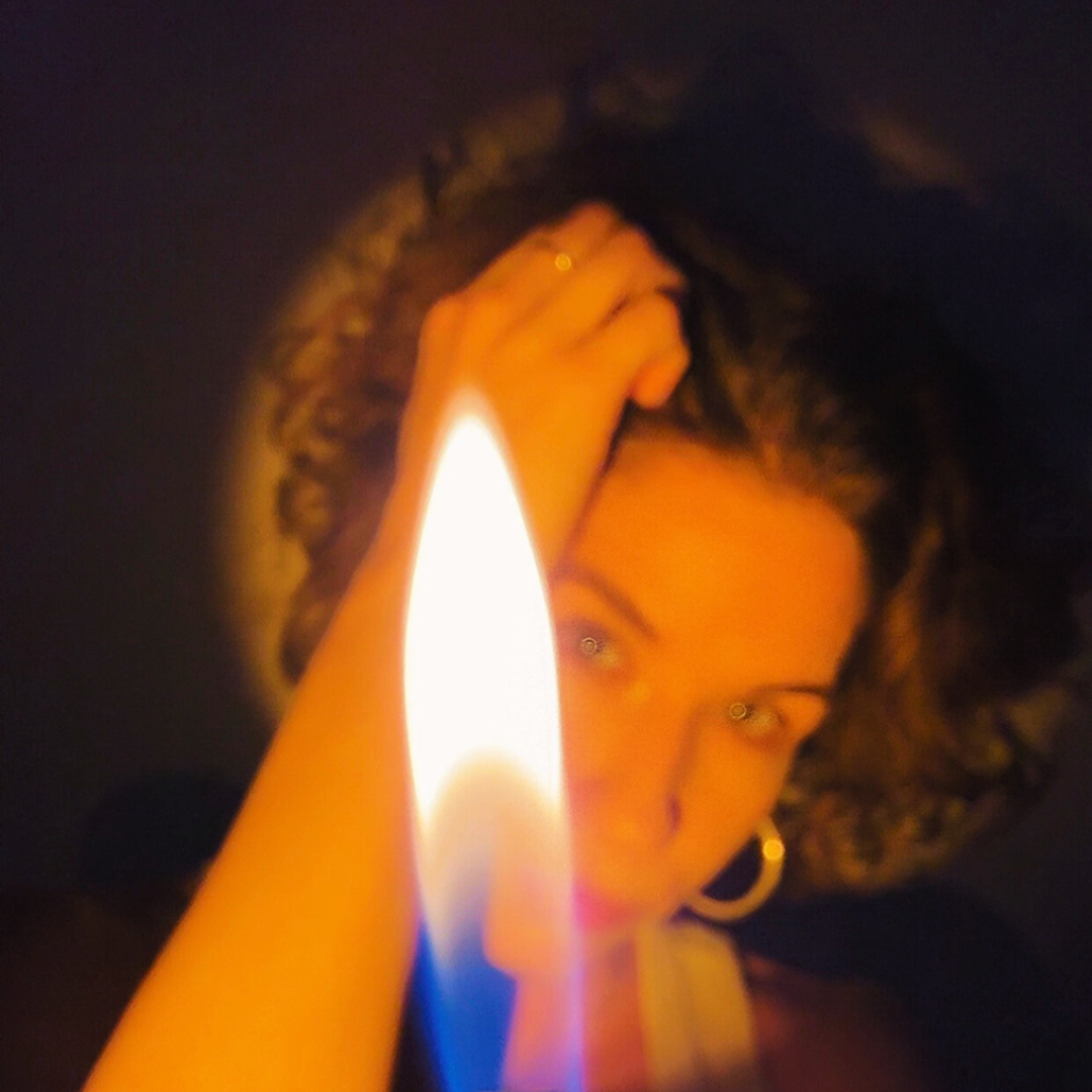 Woman holding a lit candle in front of her face, with her eyes and facial features partially illuminated by the candlelight.
