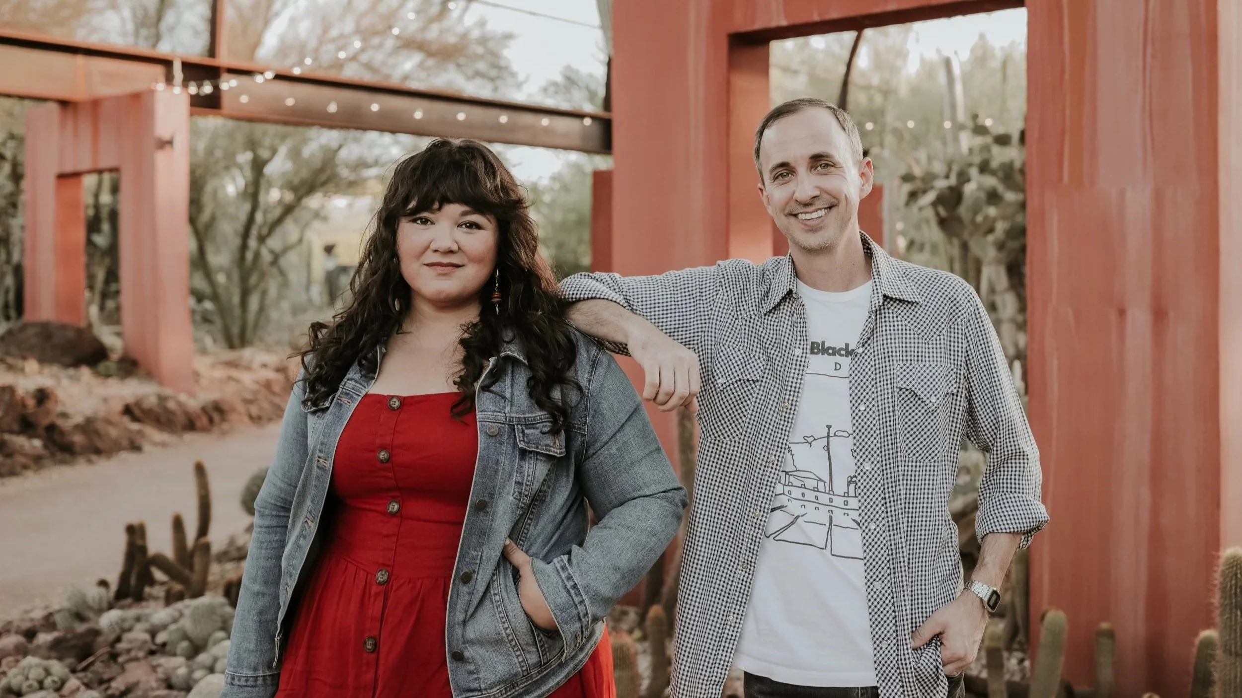 Chris Corak and Rebekah Baggs, smiling at the camera, with greenery and cacti in the background.
