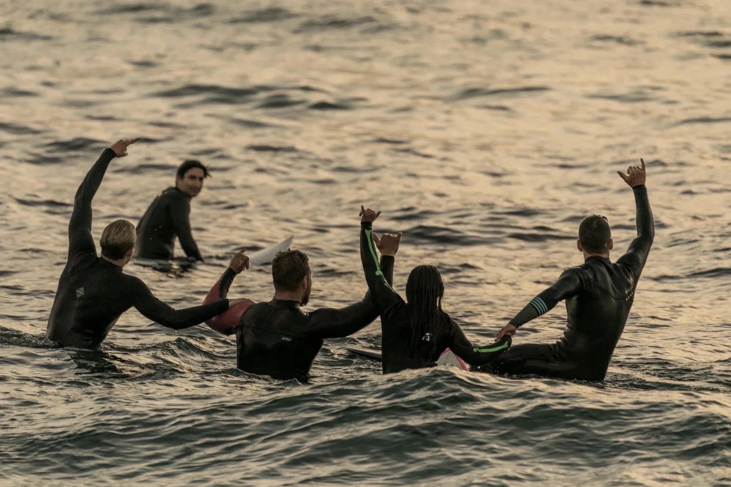 Groupe de personnes en combinaison de plongée, levant les bras dans l'eau lors d'une activité de plongée à la mer au coucher du soleil.
