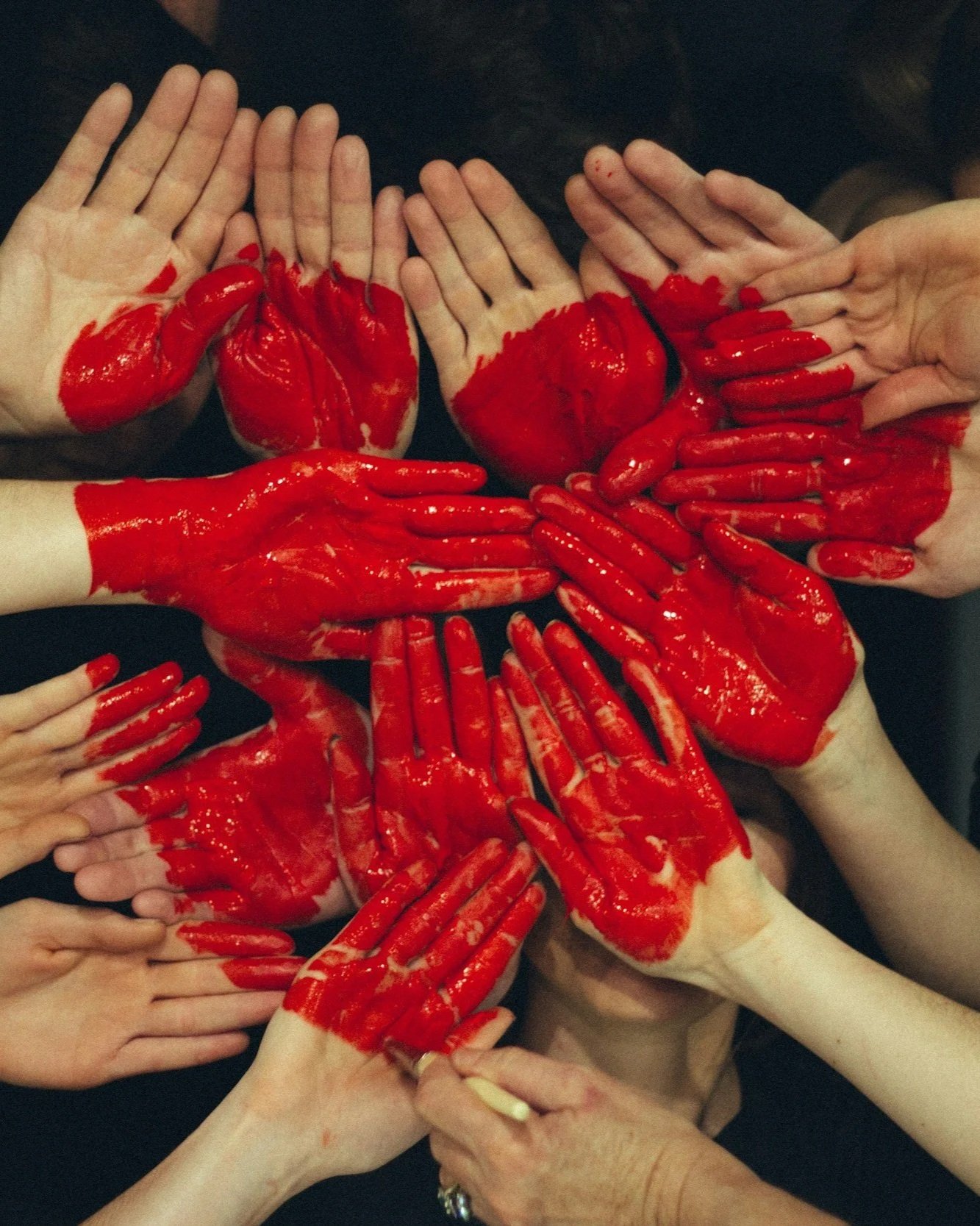 Multiple hands covered in red paint, forming a heart shape to show their love of community and support