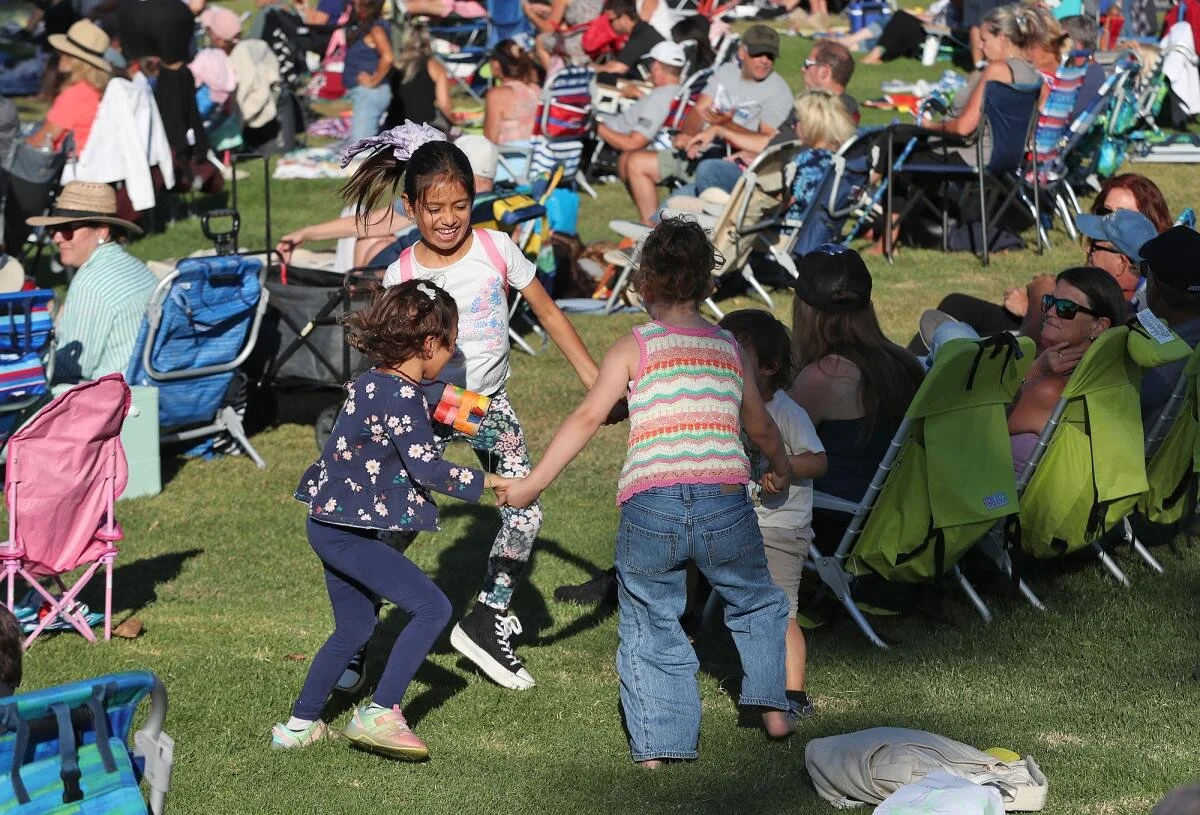 Children holding hands and playing together on a grassy field at costa mesa foundations concert in the park series