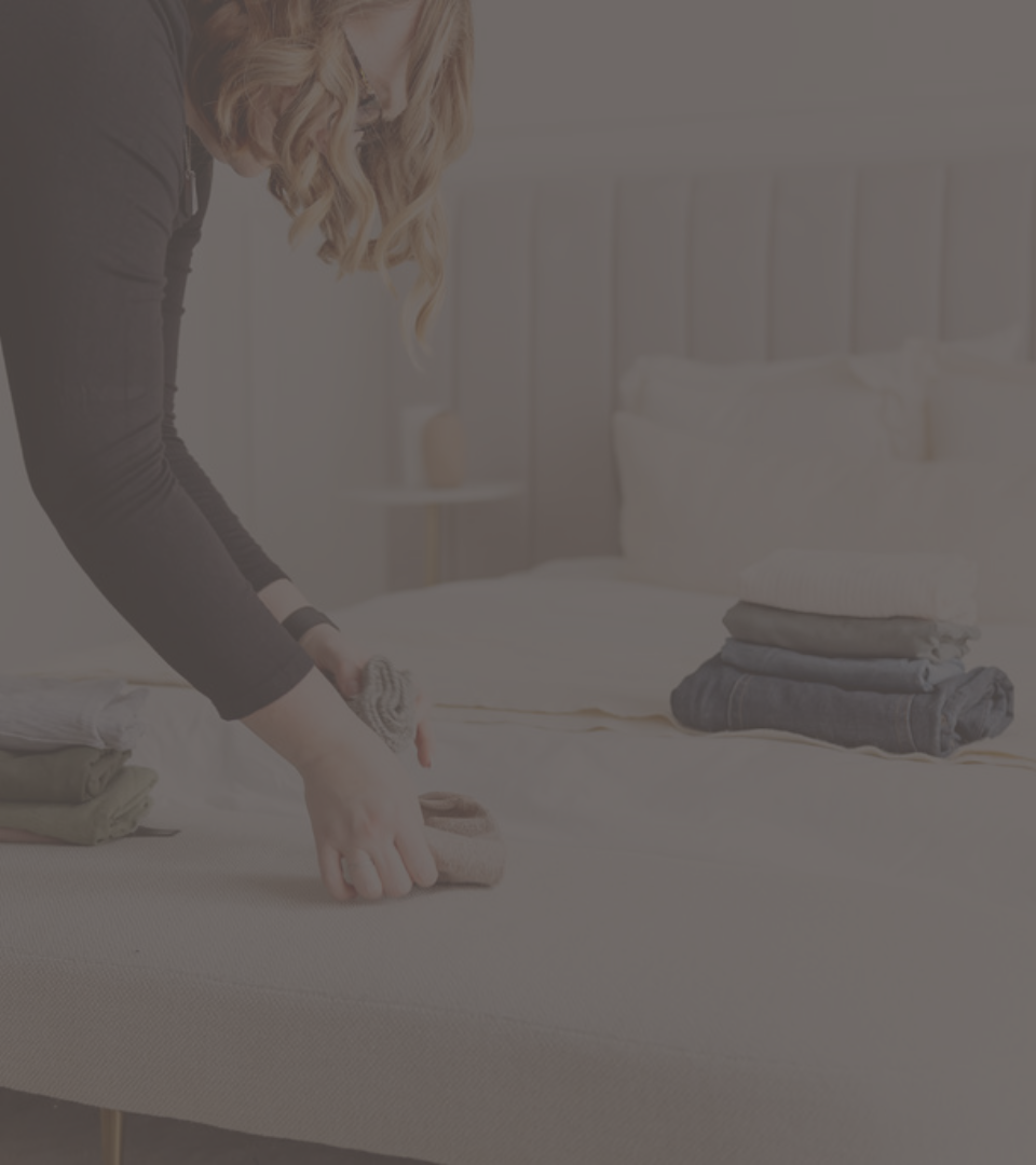Person arranging folded clothes on a bed