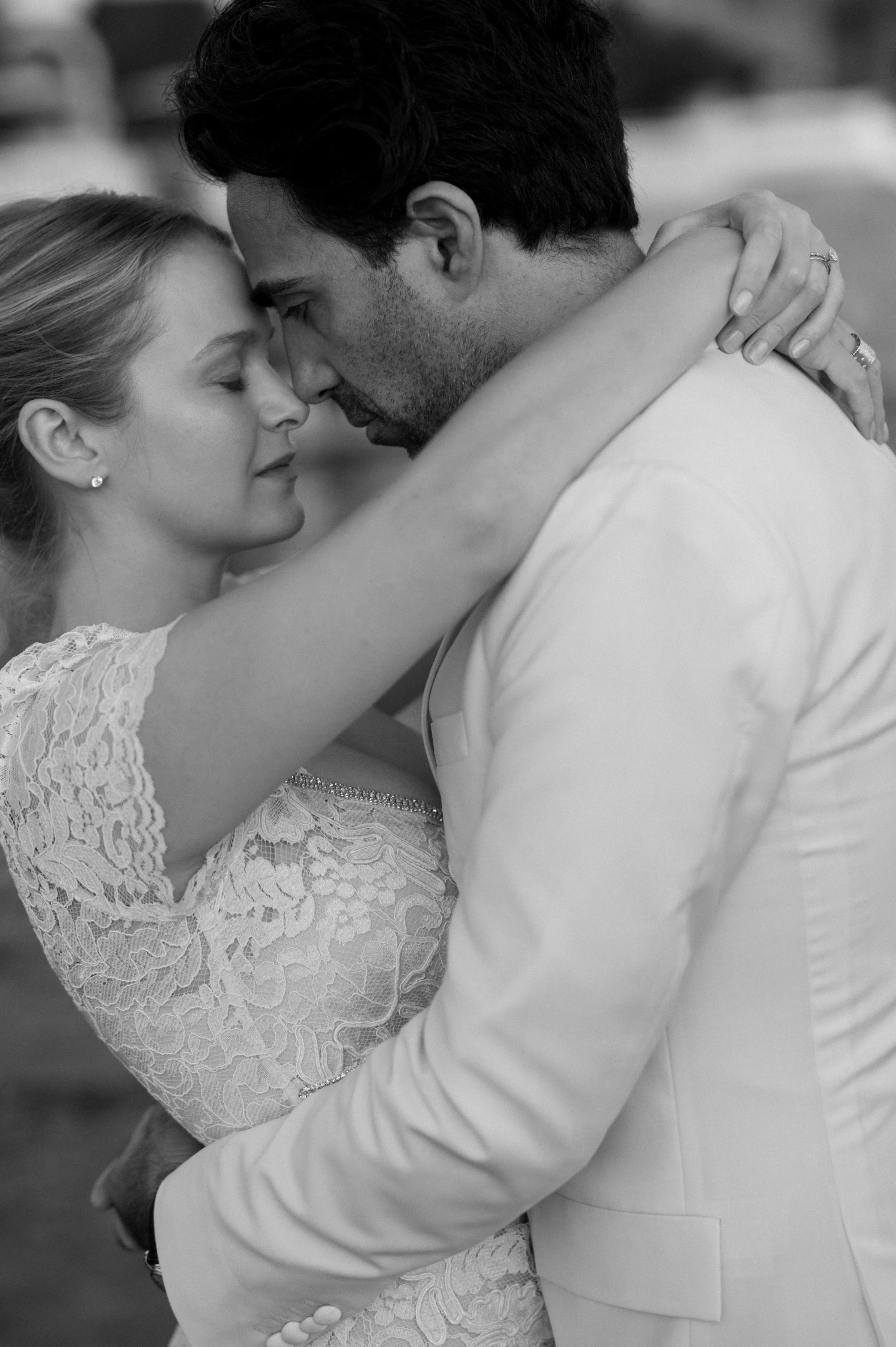 A black-and-white photo of a couple embracing closely with foreheads touching, eyes closed, appearing tender and intimate.