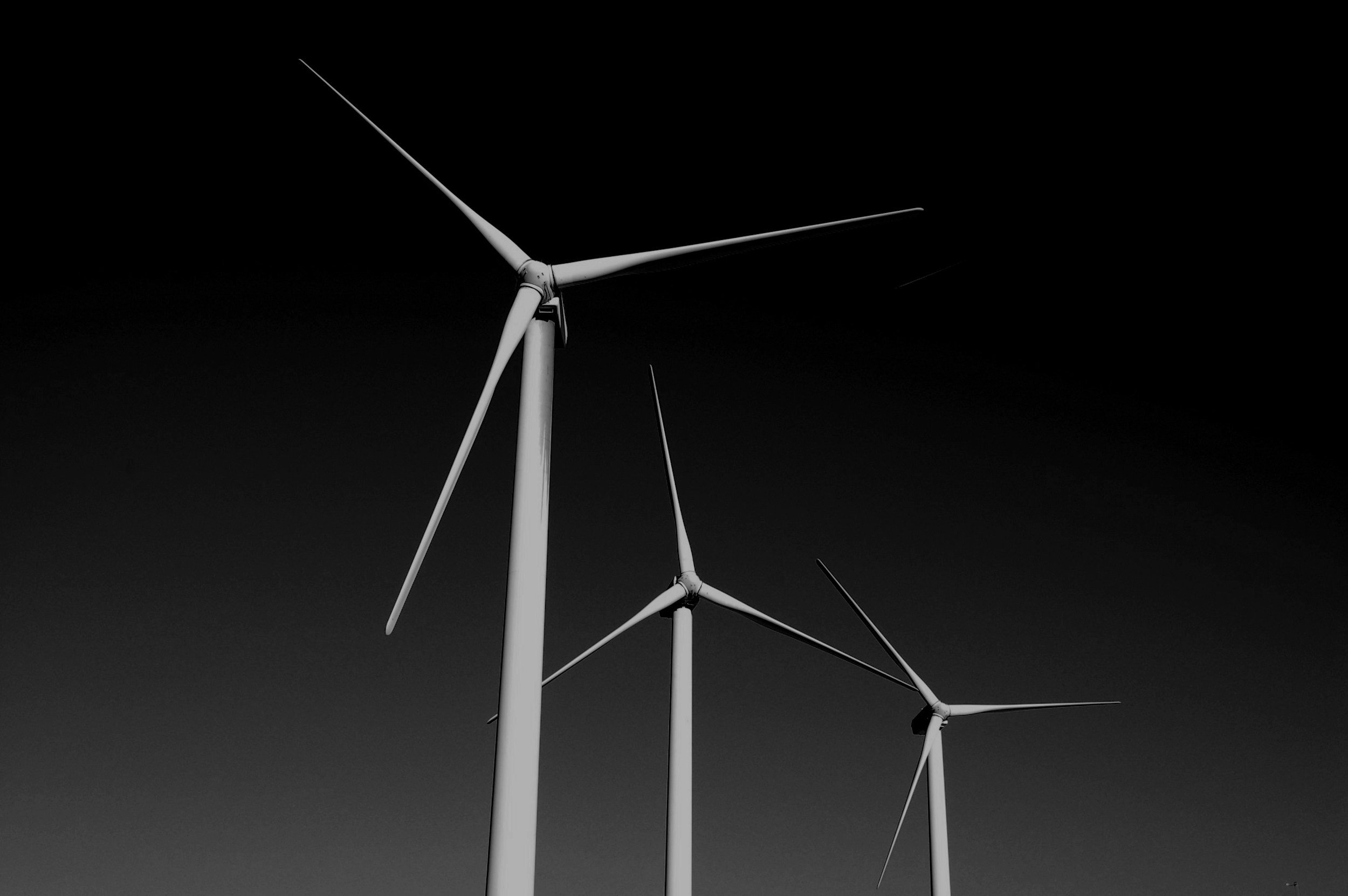 Three wind turbines against a dark sky, viewed from below.