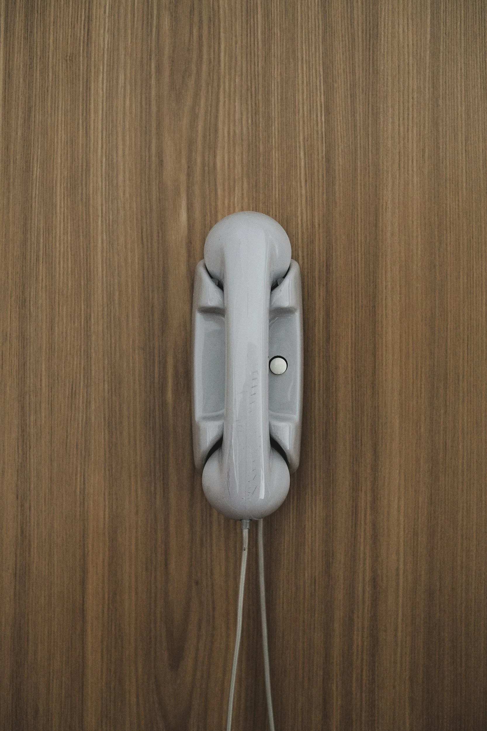 A white landline telephone mounted on a wooden wall.