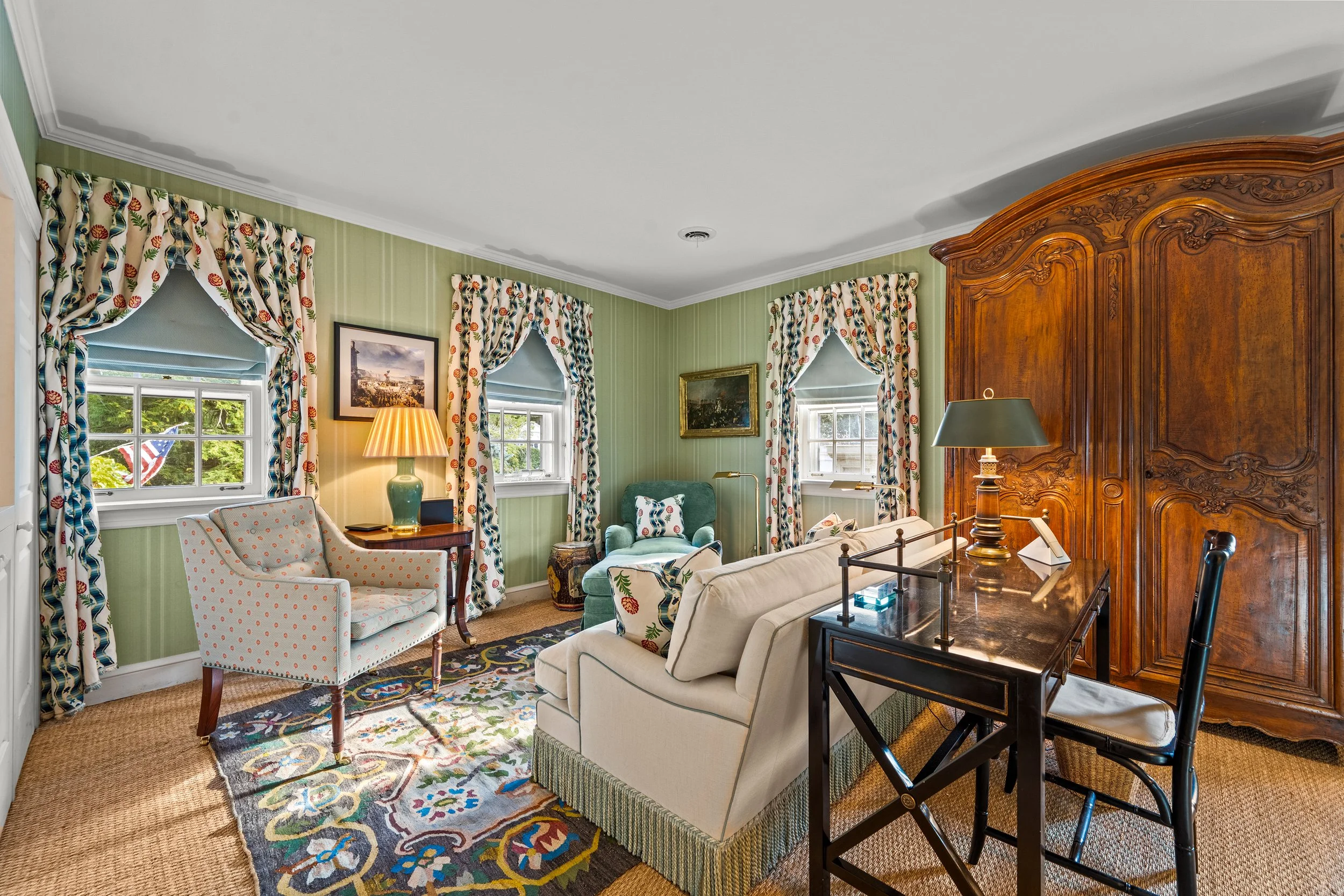 Living room with green walls, patterned curtains, a white sofa, a green armchair, and a large wooden armoire.