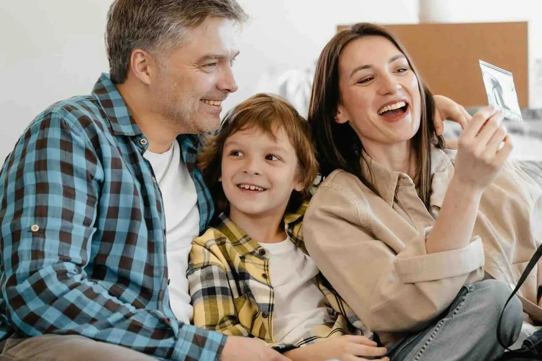 A family of three sitting on a couch, feeling happy about their new storm-safe home and business after installing hurricane impact windows and doors with Ambassador.