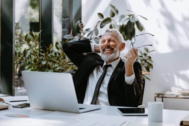 An older business executive sits at the desk of his commercial property happy about his impact windows and doors in Tampa commercial building