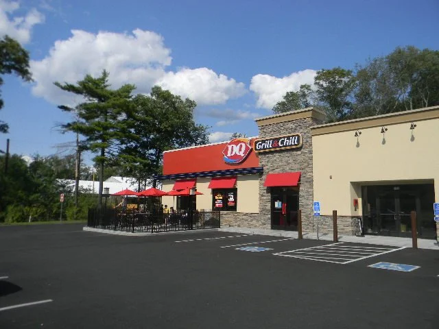 Dairy Queen restaurant with outdoor seating area, red umbrellas, and a parking lot.