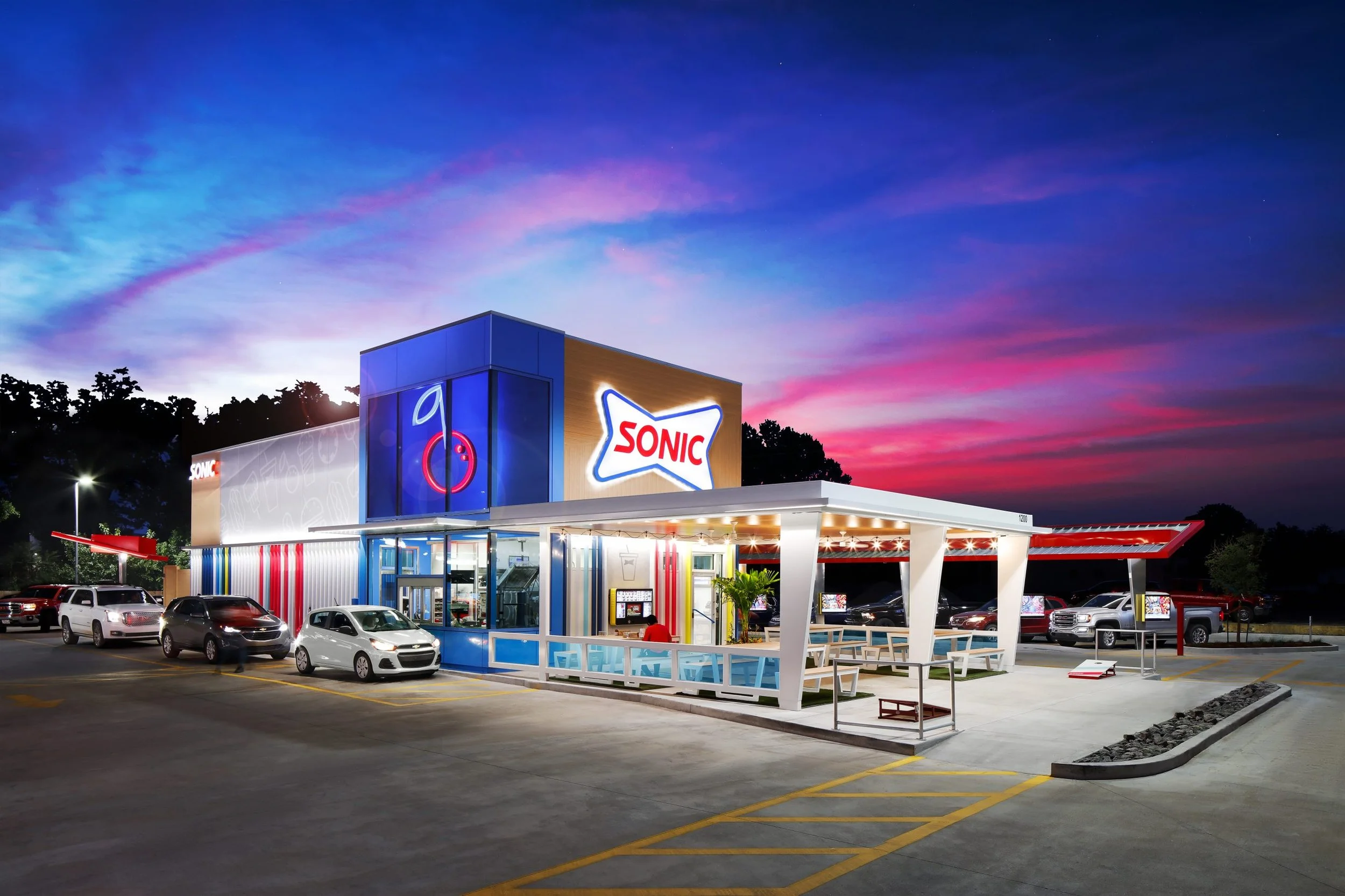 Sonic fast-food restaurant at dusk with colorful sky, parking lot, and cars in front.