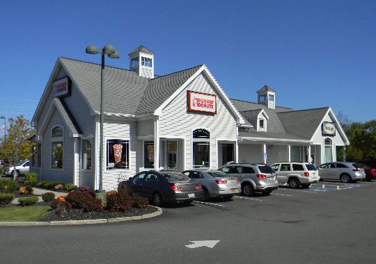 Chick-fil-A restaurant with a parking lot filled with cars, clear blue sky, and some trees and landscaping in front.