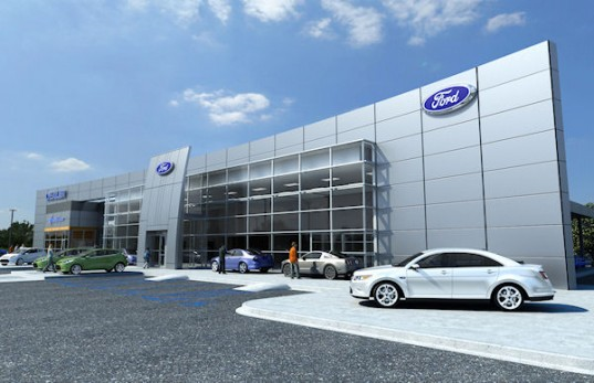 Exterior view of a Ford car dealership with several cars parked in front and large glass windows.