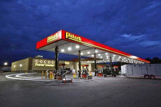 Pilot travel center gas station with illuminated canopy, cars, and a travel center building at dusk.