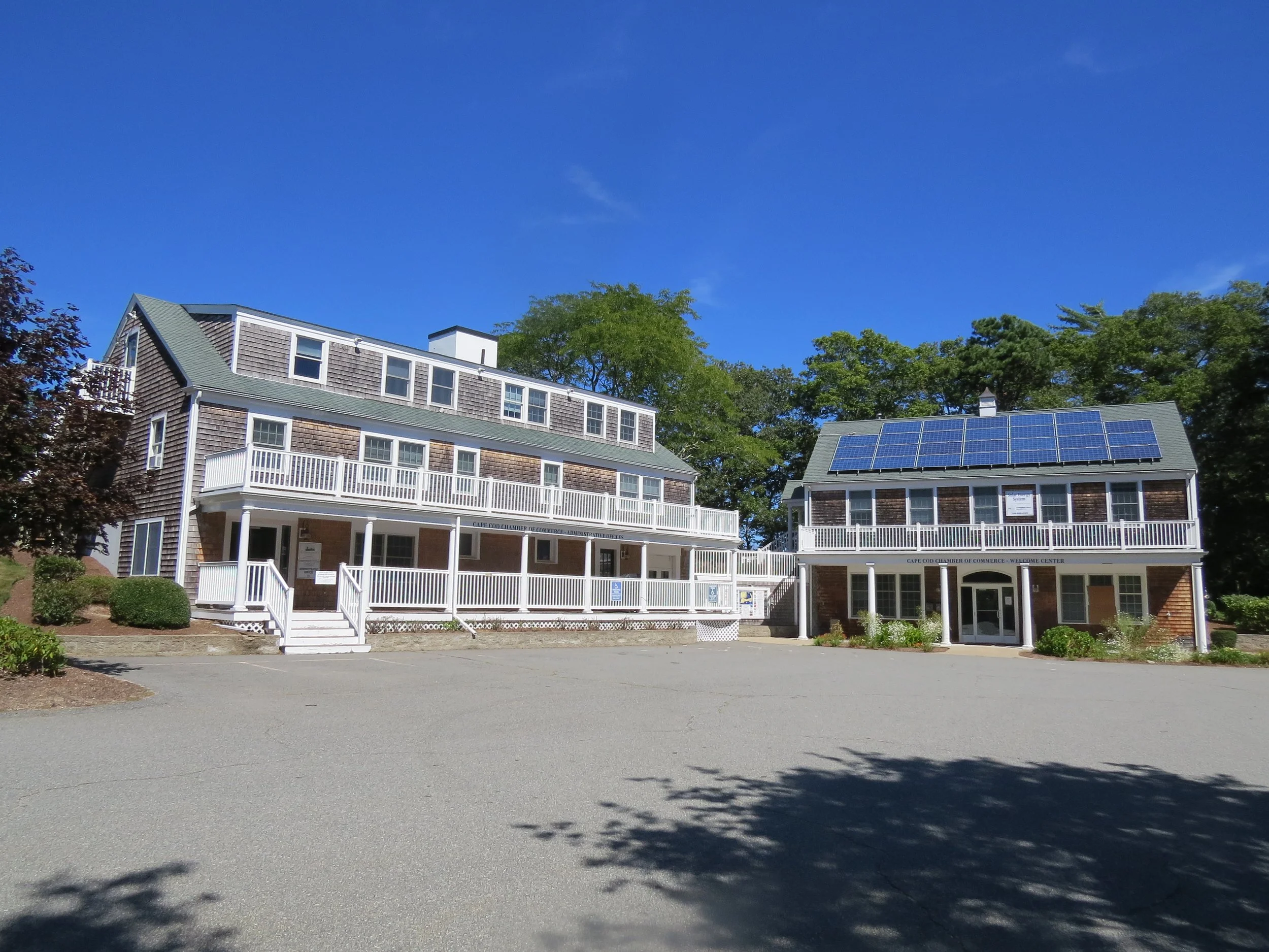 Two buildings with solar panels on the roof, surrounded by trees and a clear blue sky.