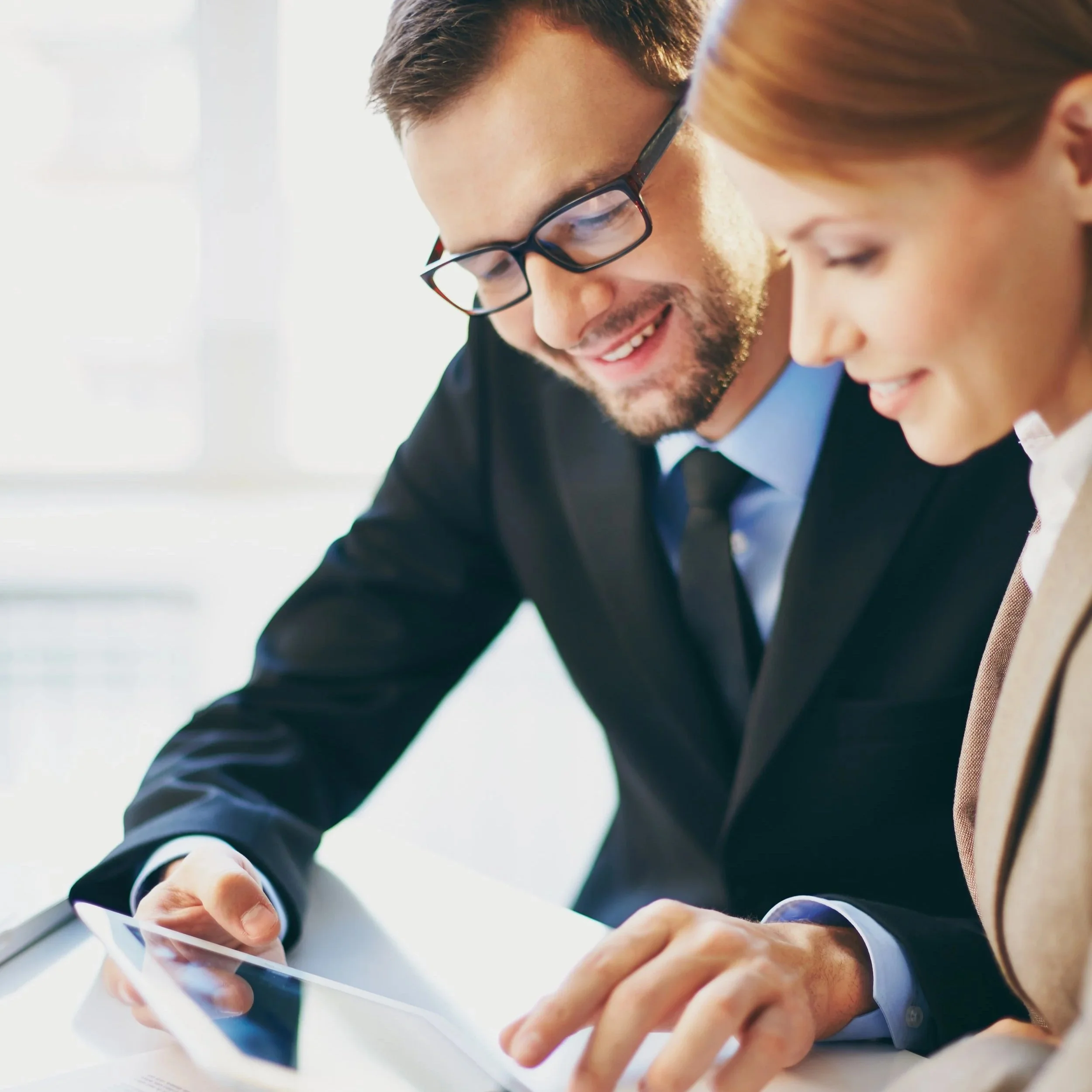 A man and woman in business attire looking at a tablet together in an office setting.