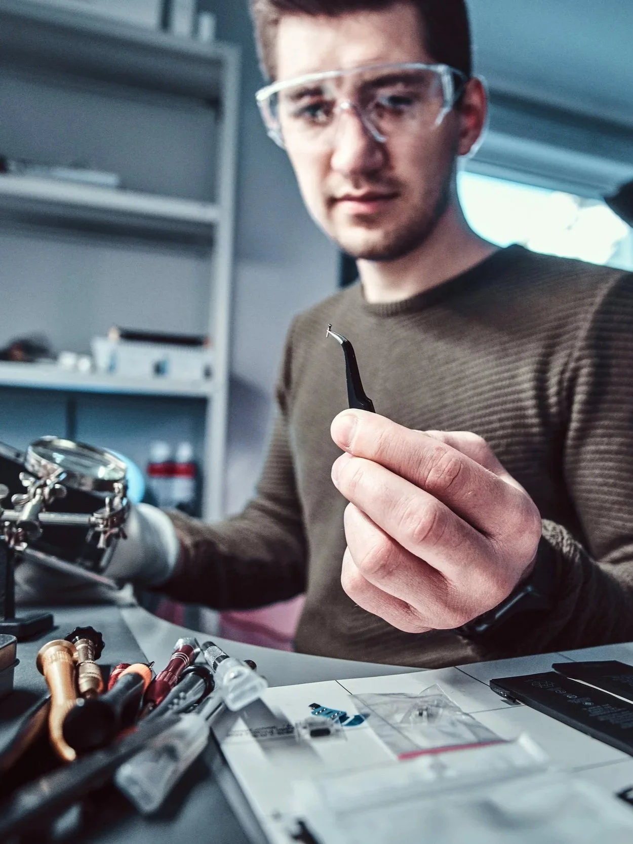 A man in safety glasses holding a dental tool inside a dental laboratory.