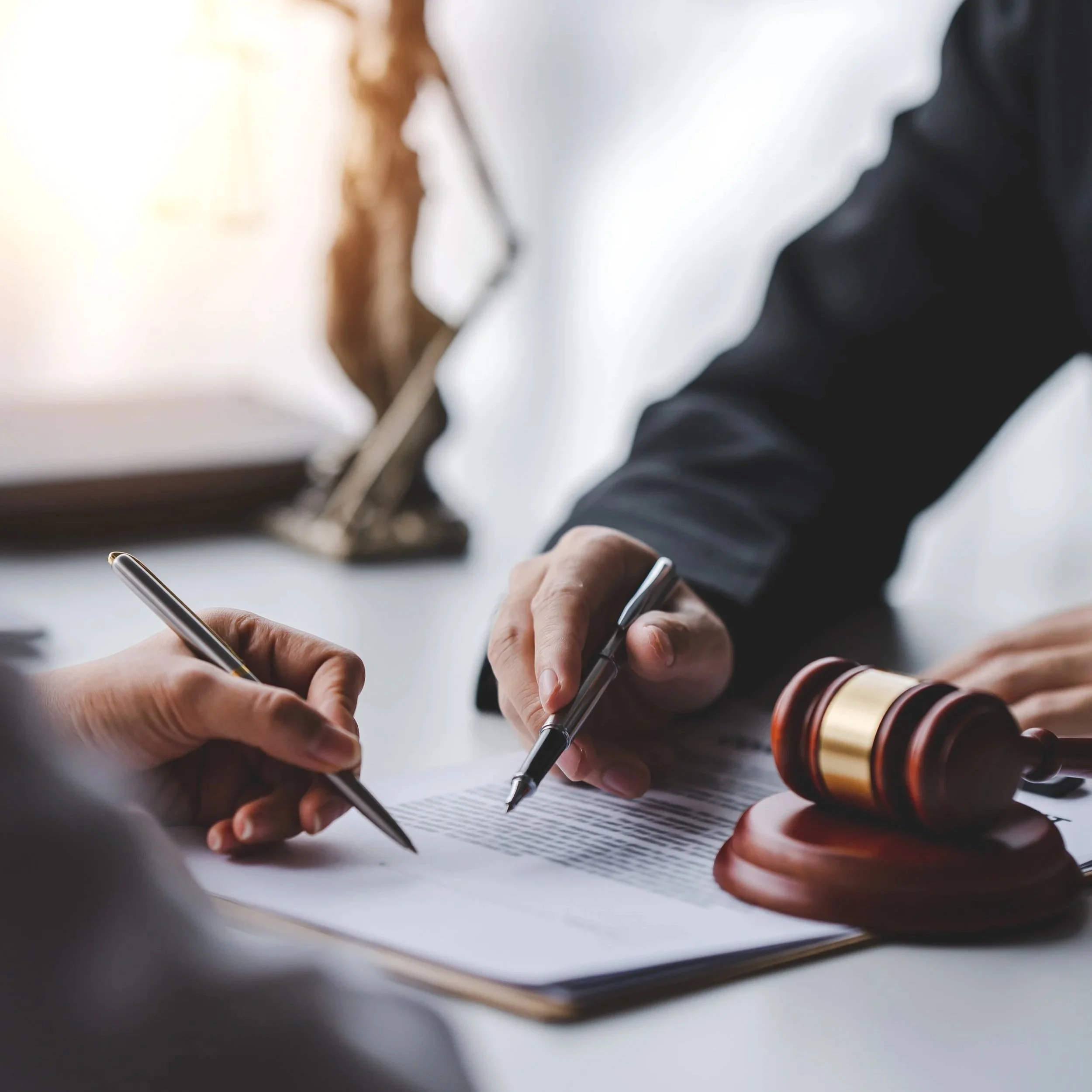 Close-up of a legal signing with a judge's gavel on a table, a person holding a pen, and another person signing a document.