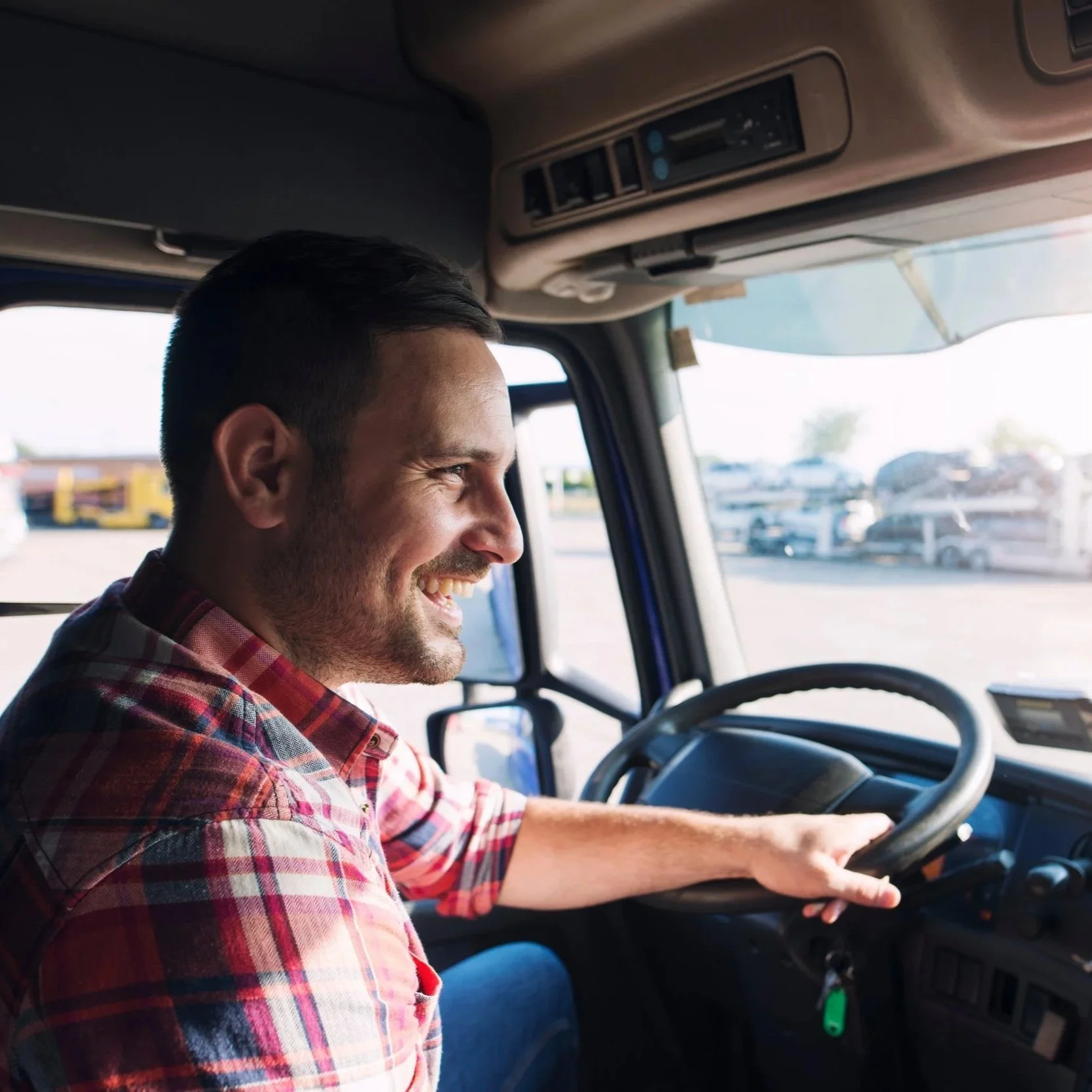 A man driving a commercial truck, smiling while holding the steering wheel.
