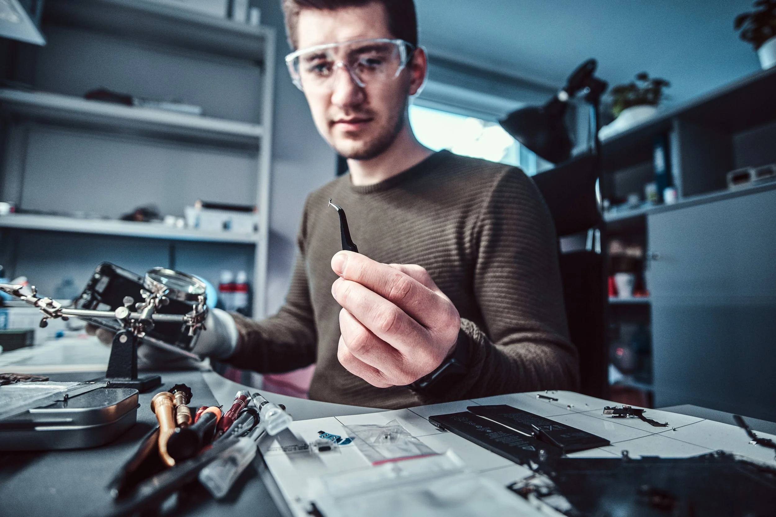 Man working on electronics at a cluttered desk with tools and electronic parts.