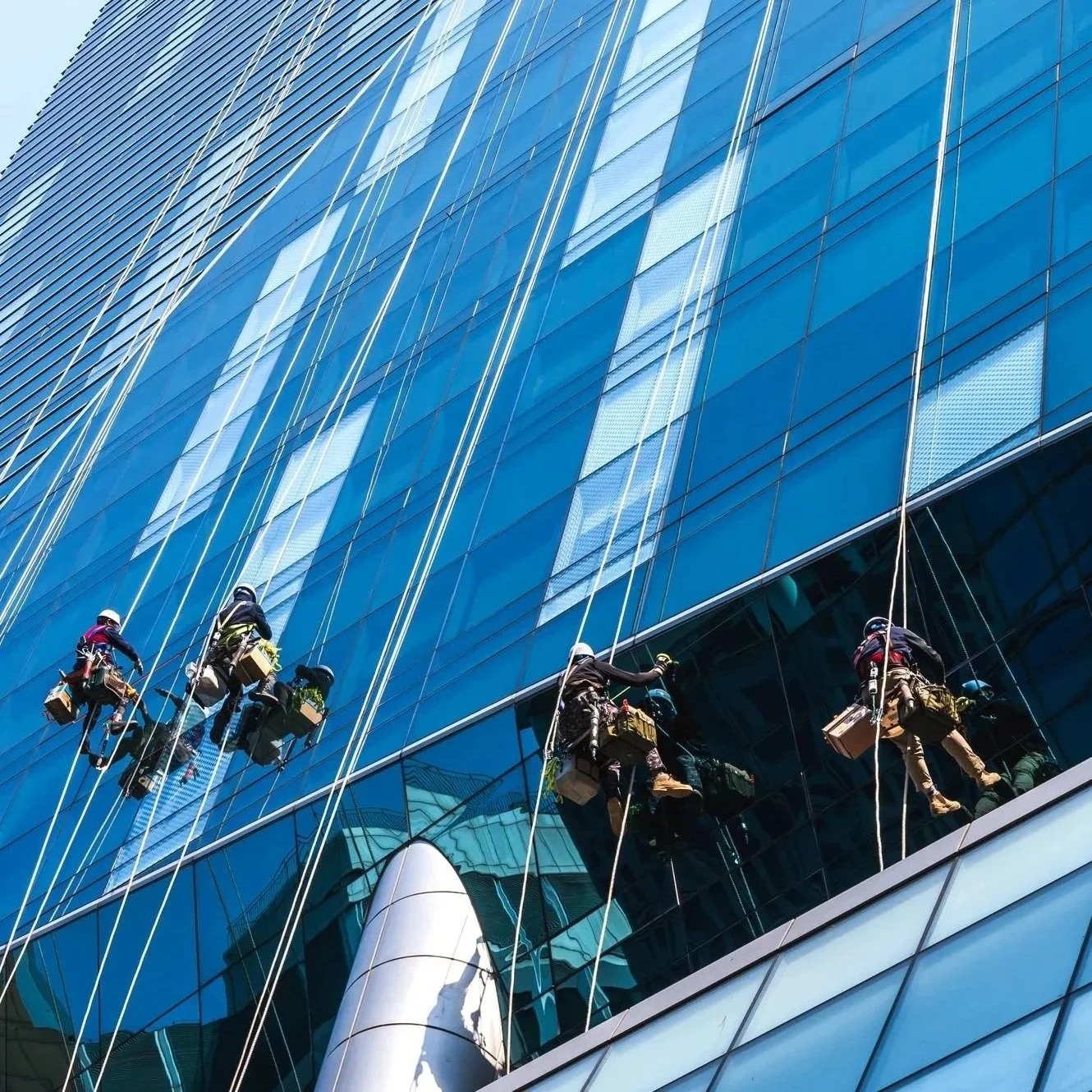 Window washers cleaning the glass exterior of a modern glass building.
