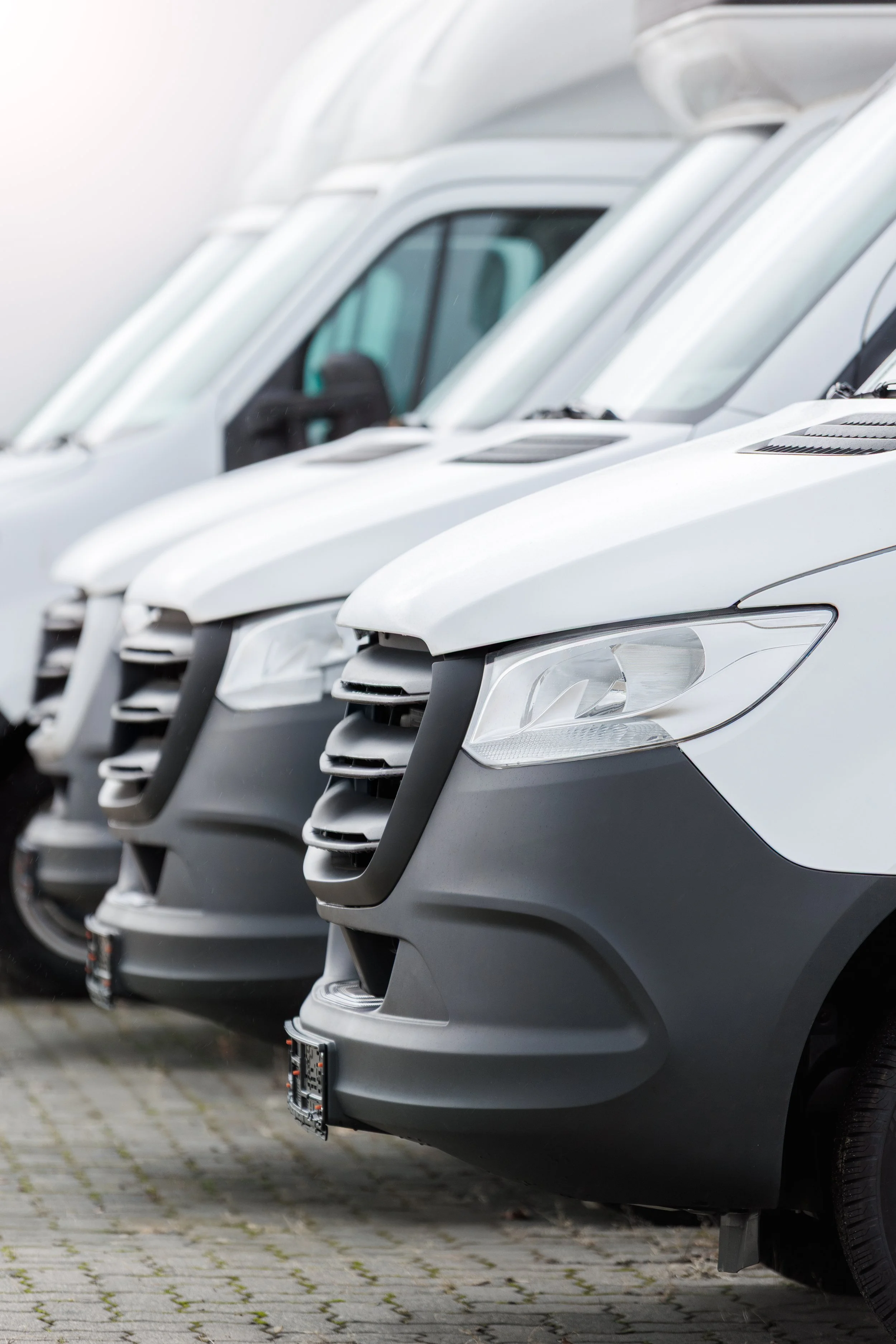 Multiple white commercial vans parked in a row on a paved surface.