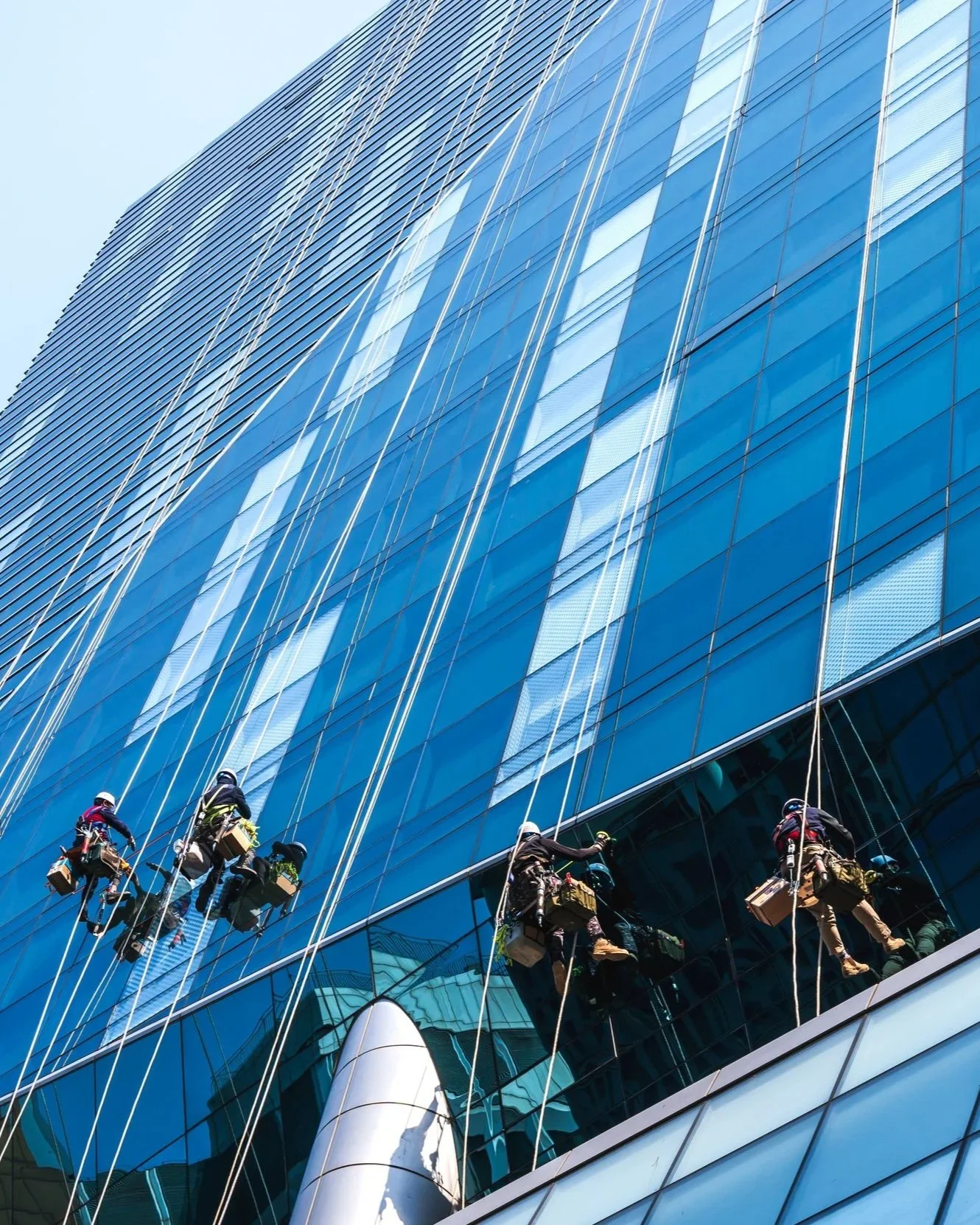 Window cleaners suspended on ropes cleaning the glass exterior of a tall modern skyscraper.