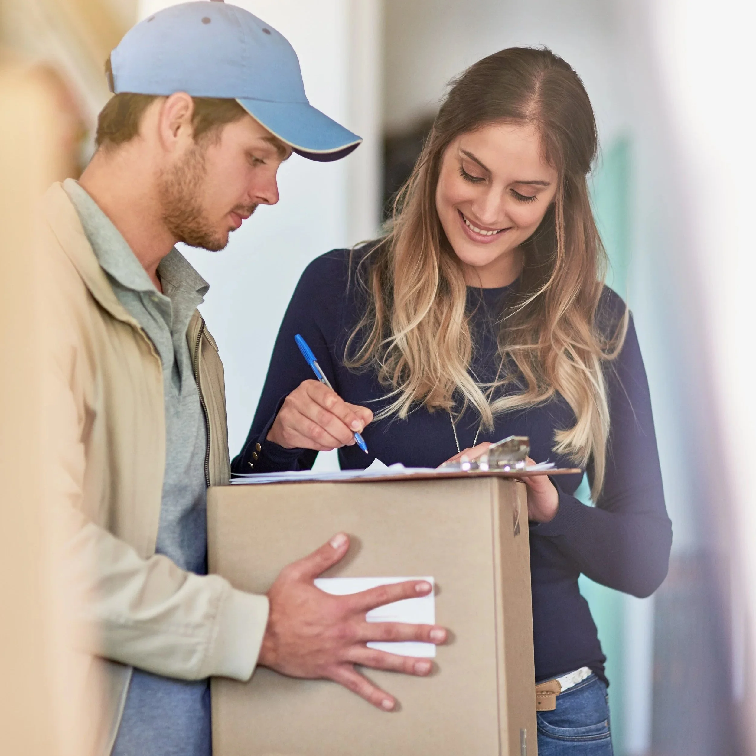 A man and woman are smiling and looking at a clipboard and a box, possibly during a delivery or check-in process.