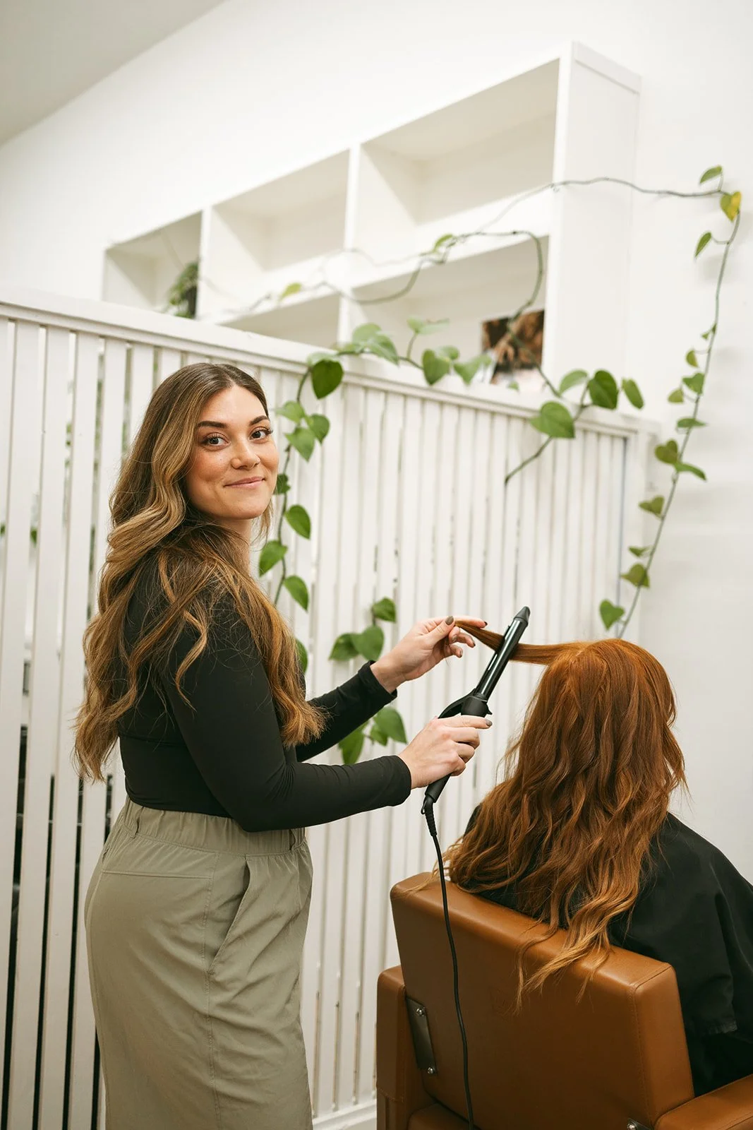 Destinee Horat styling a client's long hair with a curling iron in her Lynden salon